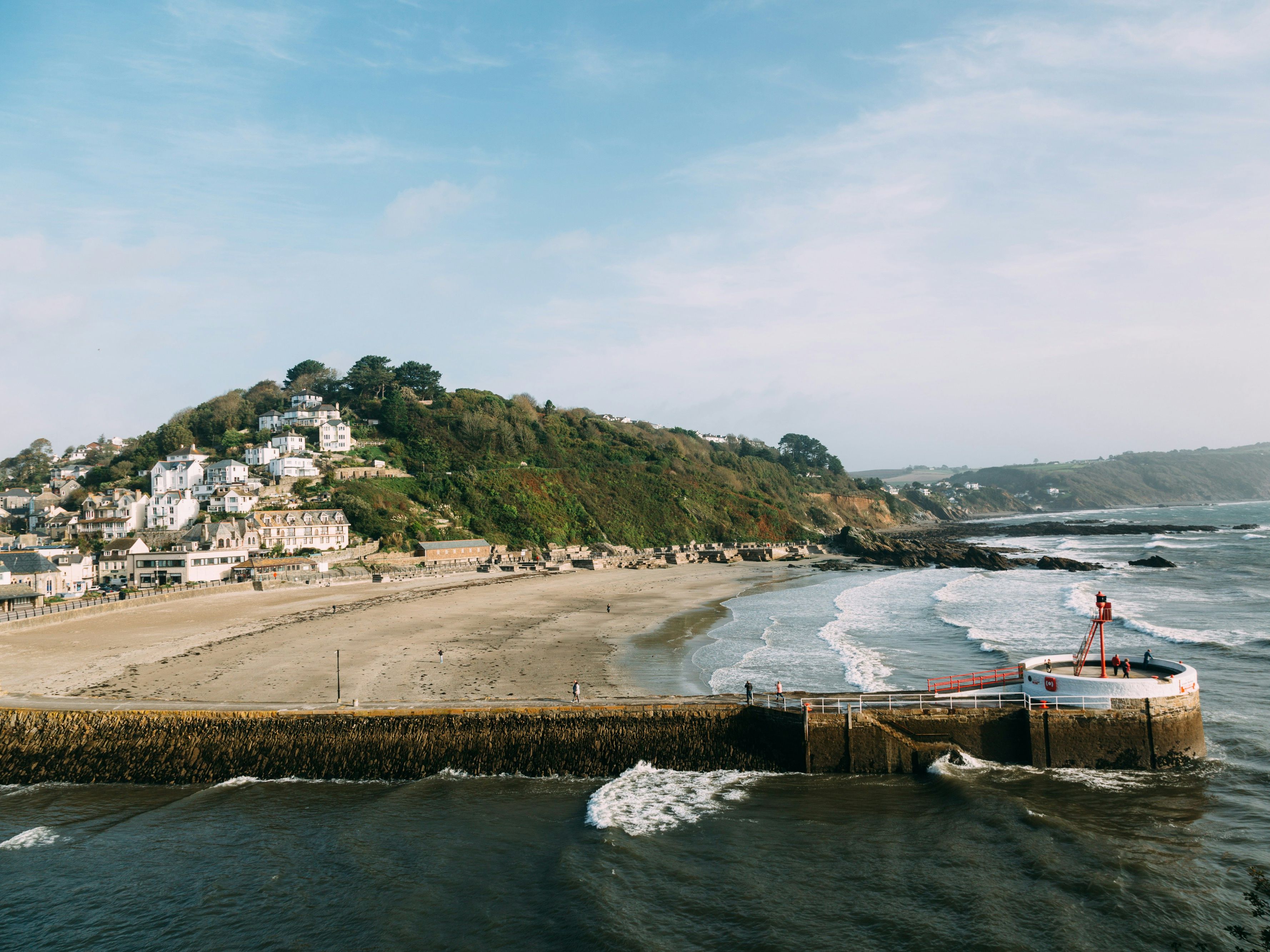 Coastal village with houses on a hill overlooking a sandy beach and a pier extending into the sea.