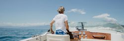 Person steering a boat on a sunny day with ocean and blue sky