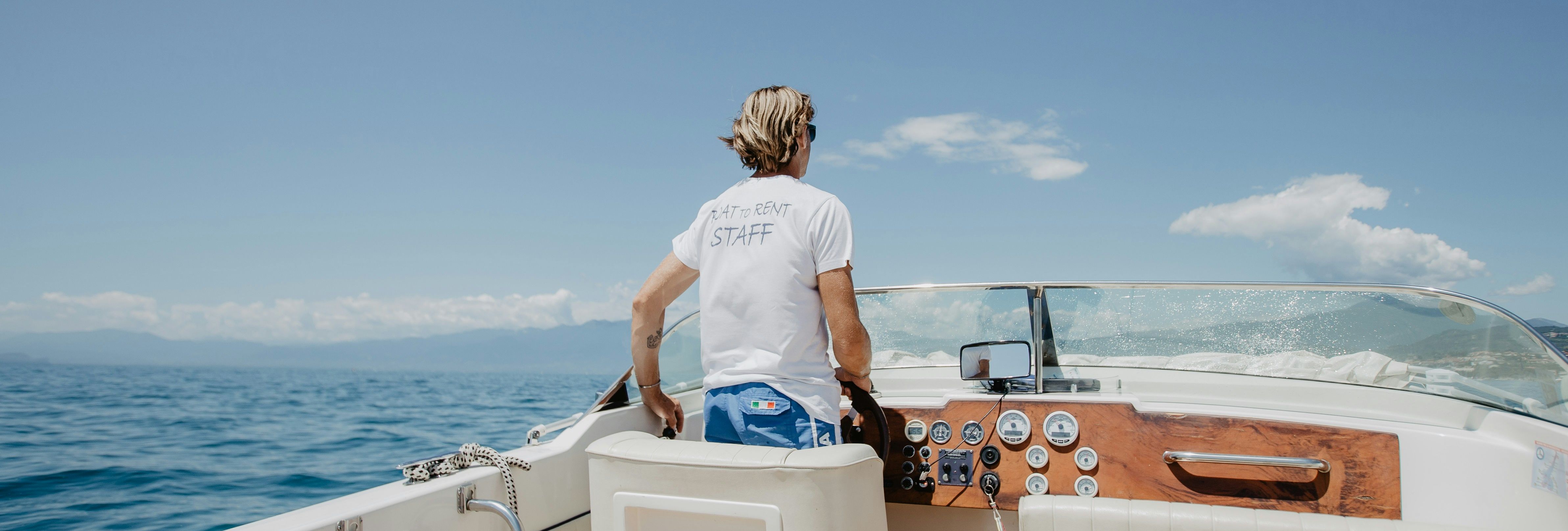 Person steering a boat on a sunny day with ocean and blue sky