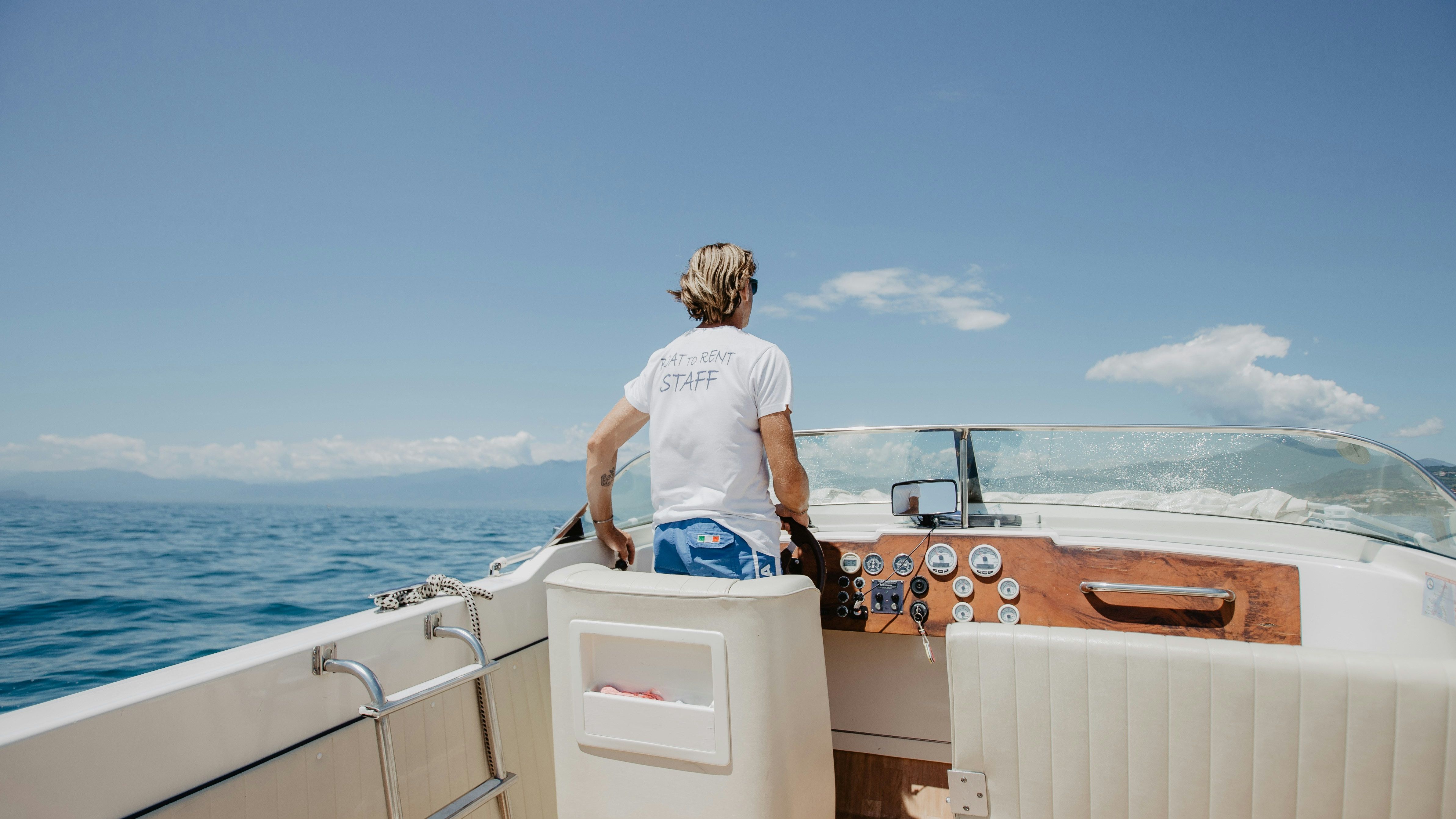 Person steering a boat on a sunny day with ocean and blue sky
