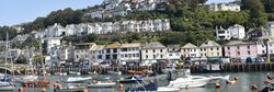 Boats docked at a harbor with a hillside town in the background under a clear blue sky