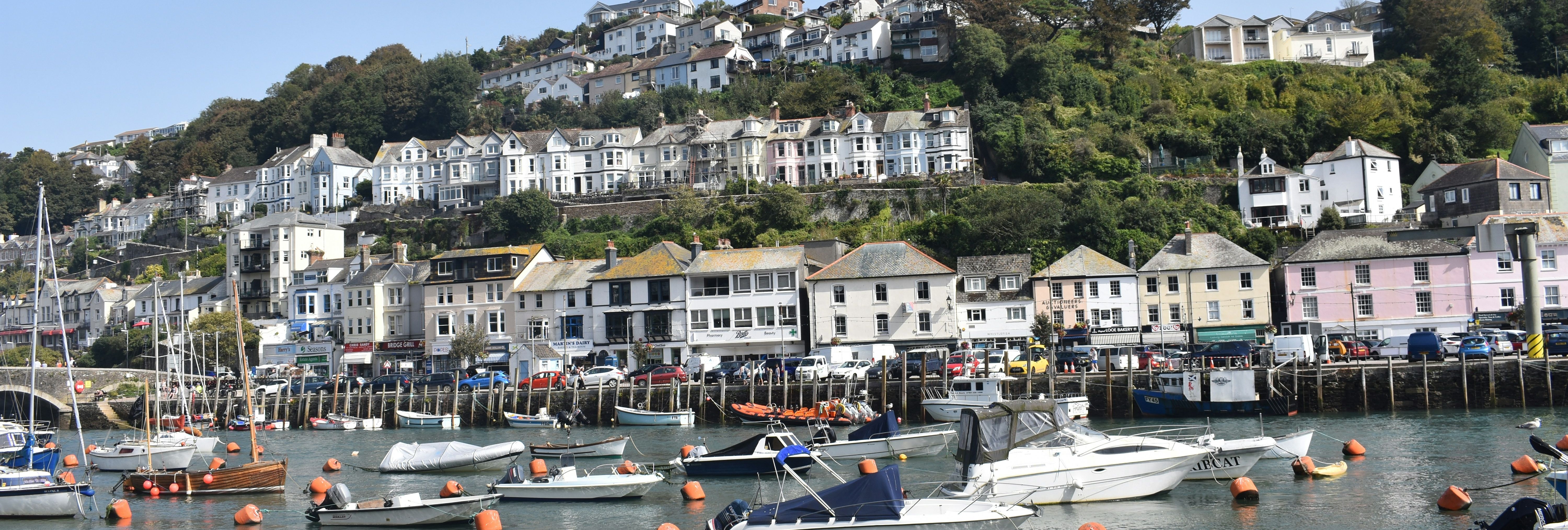 Boats docked at a harbor with a hillside town in the background under a clear blue sky
