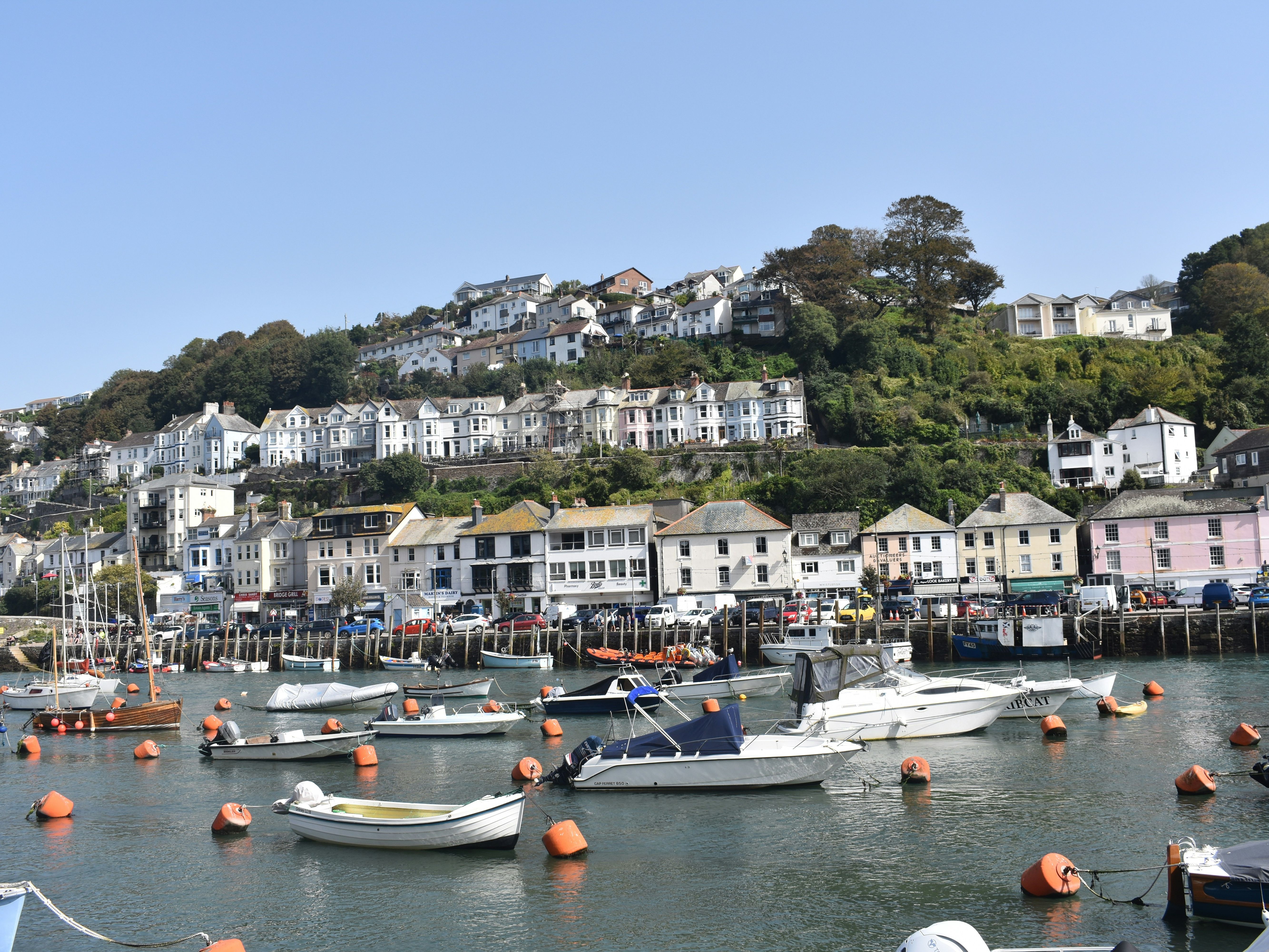 Boats docked at a harbor with a hillside town in the background under a clear blue sky