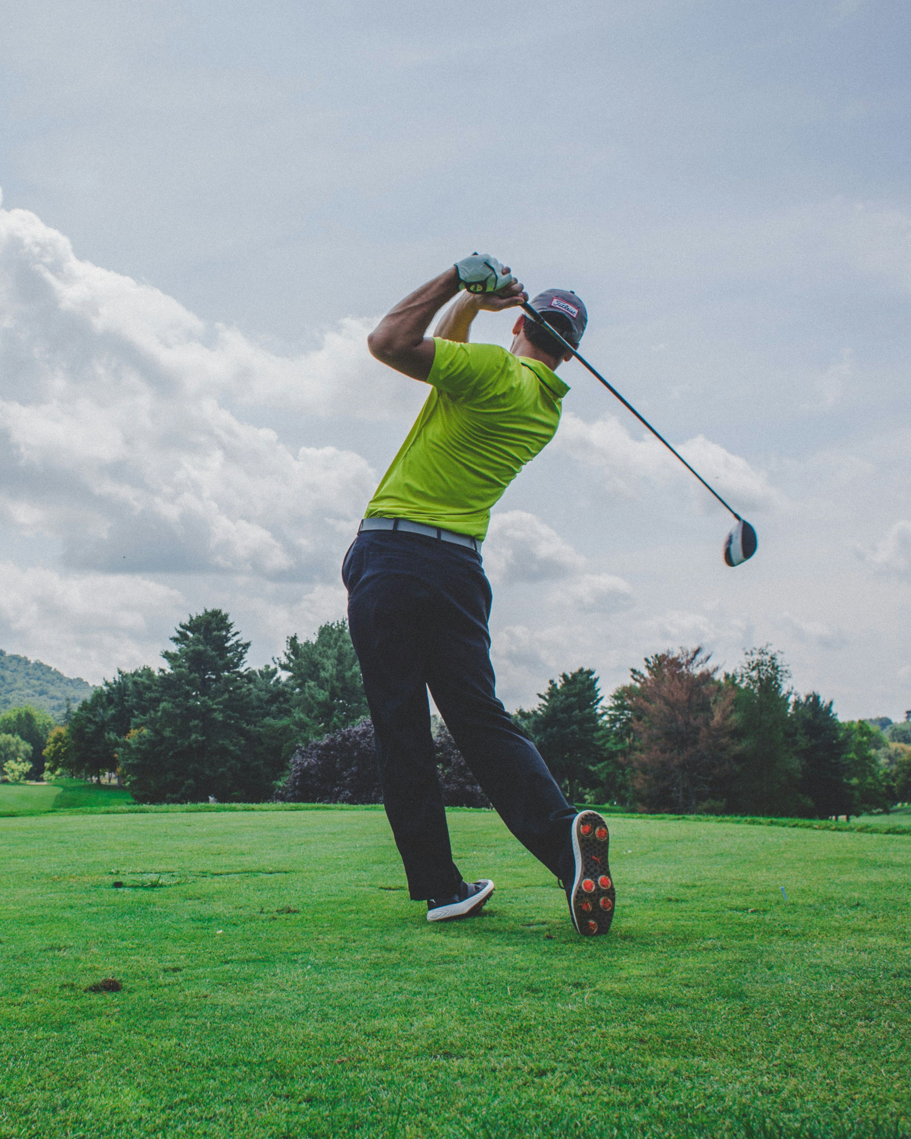 Golfer in a yellow shirt taking a swing on a lush golf course with trees and hills in the background
