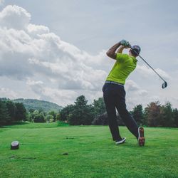 Golfer in a yellow shirt taking a swing on a lush golf course with trees and hills in the background