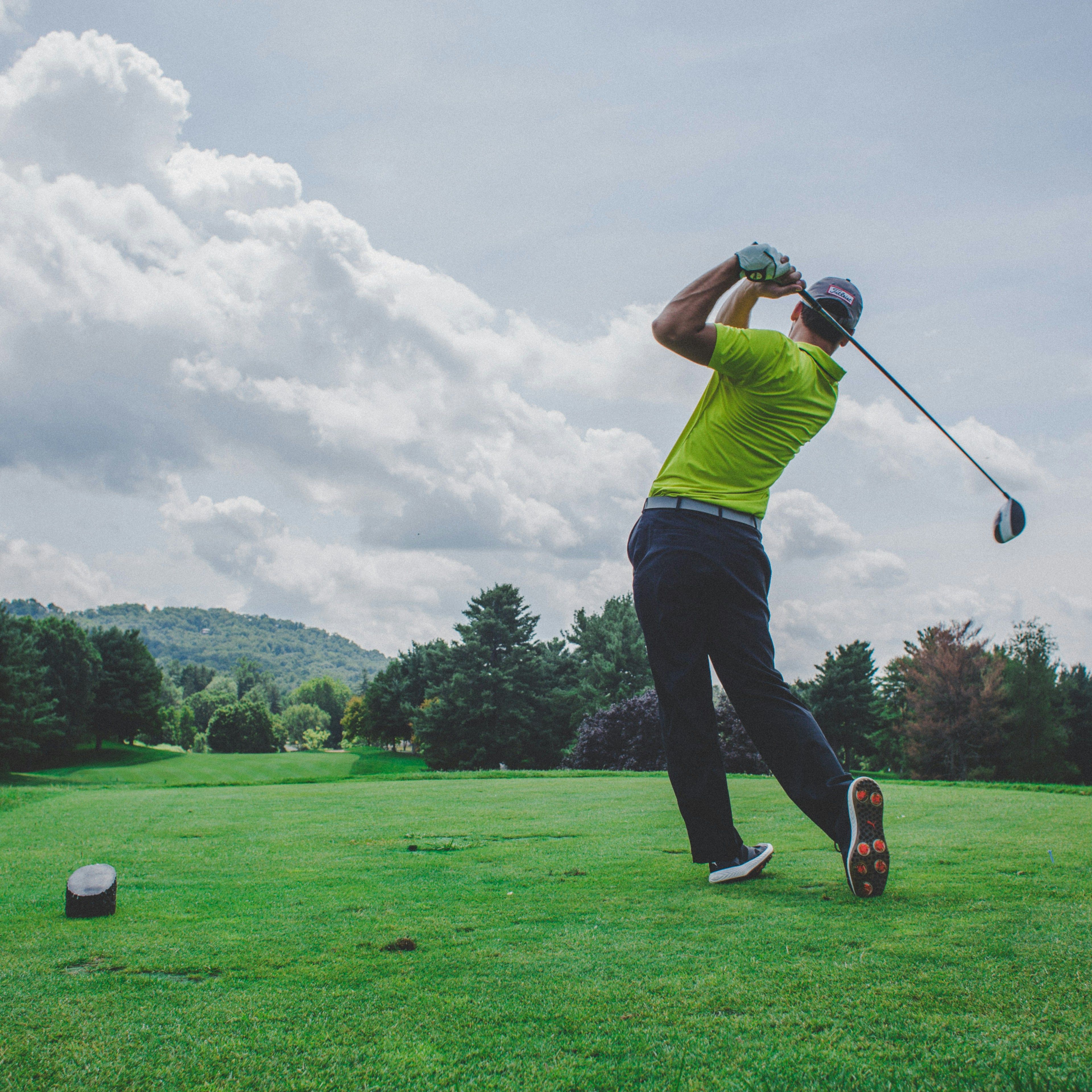 Golfer in a yellow shirt taking a swing on a lush golf course with trees and hills in the background
