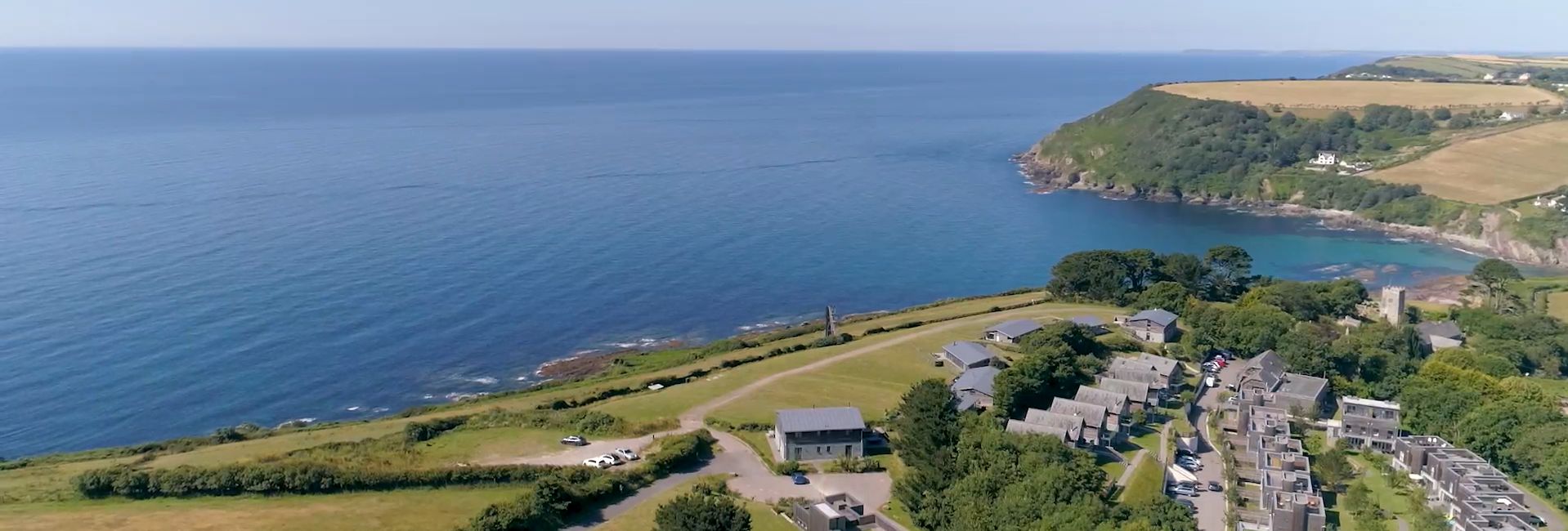 Aerial view of coastal village with houses, open fields, and the sea
