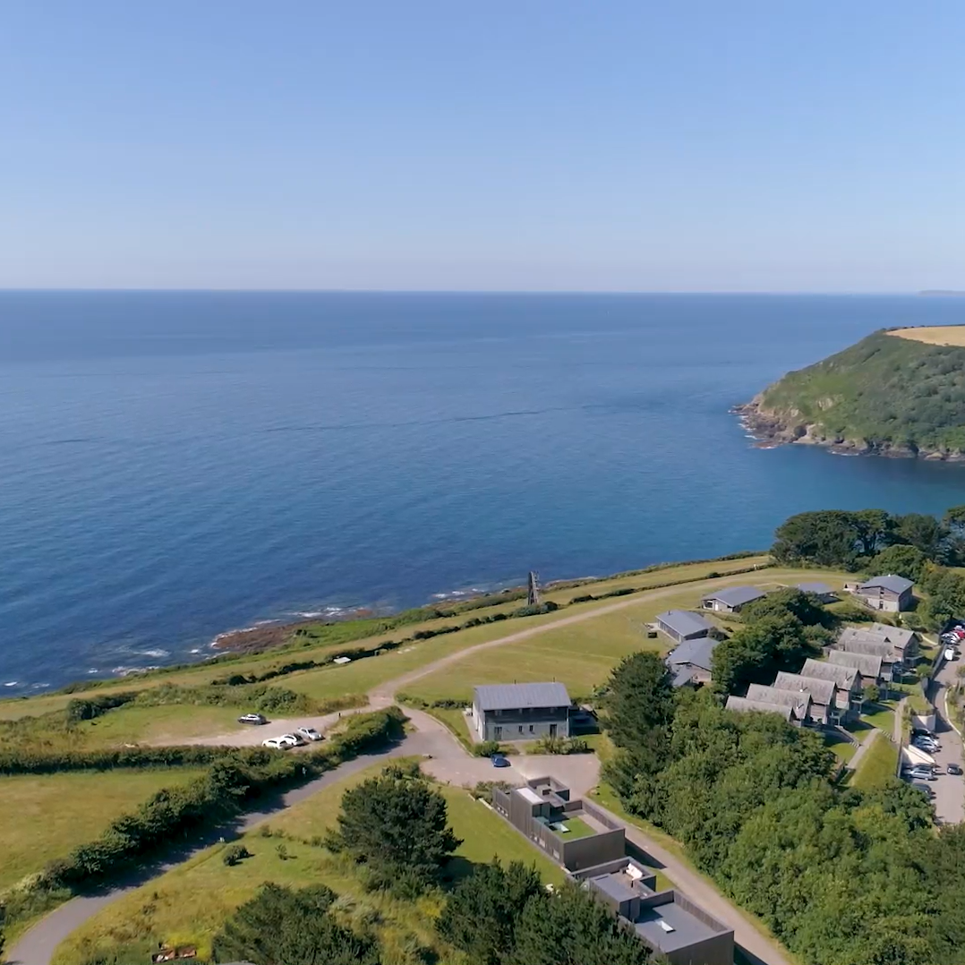 Aerial view of coastal village with houses, open fields, and the sea