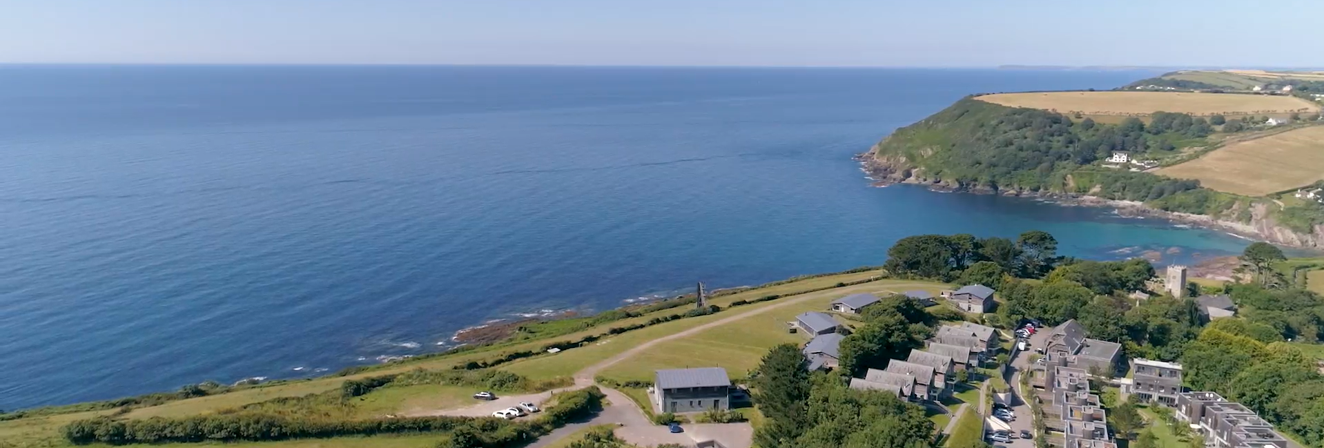 Aerial view of coastal village with houses, open fields, and the sea