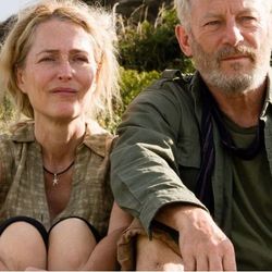 A woman and a man sitting outdoors on a grassy hillside with a backpack next to them.