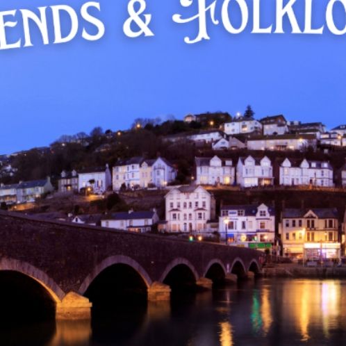 Scenic view of Looe, Cornwall at dusk with illuminated houses, a historic bridge, boats, and the title 'Legends & Folklore of Looe' at the top.