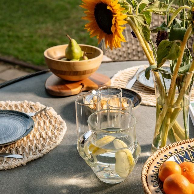 Outdoor table set with sunflowers, glass pitcher of lemon water, fruit bowls, and table settings.