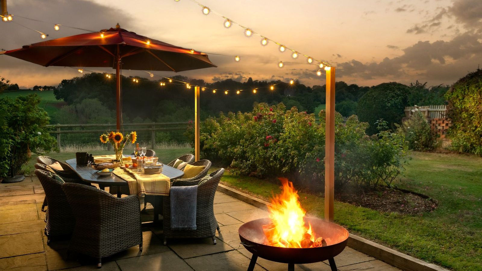 Cozy outdoor patio with a fire pit, dining table, string lights, and sunset view