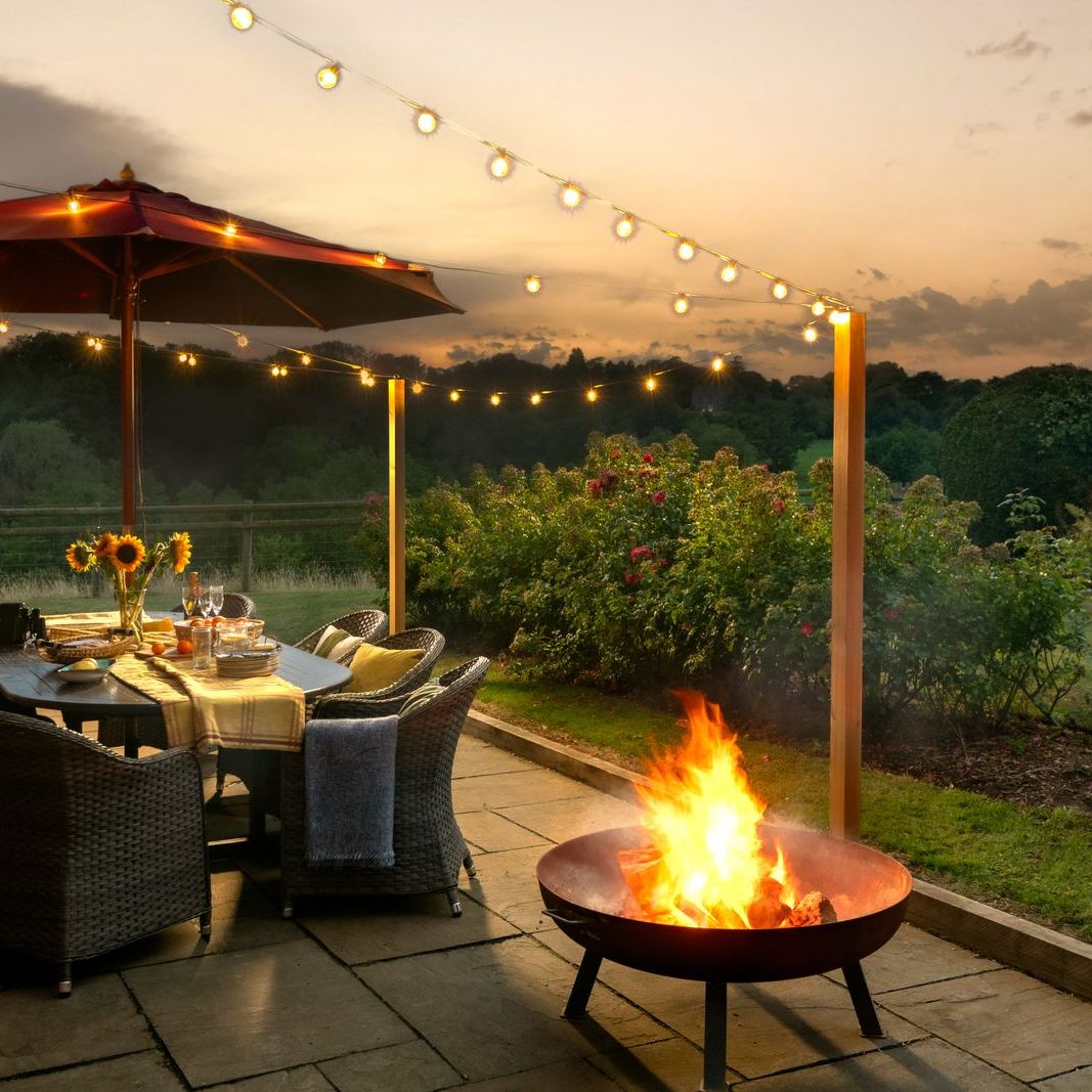 Cozy outdoor patio with a fire pit, dining table, string lights, and sunset view