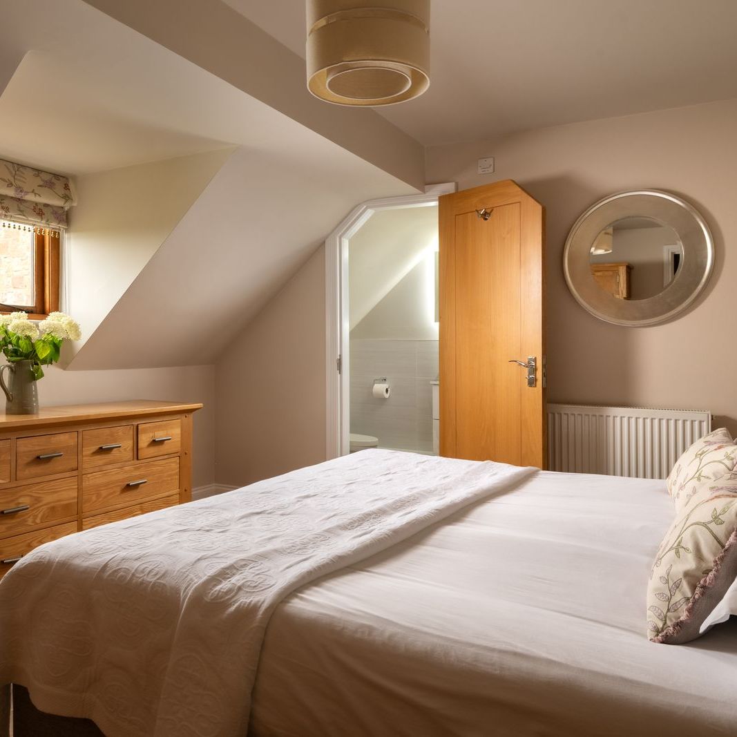 Cozy bedroom with sloped ceiling, wooden dresser, and bed with white linens