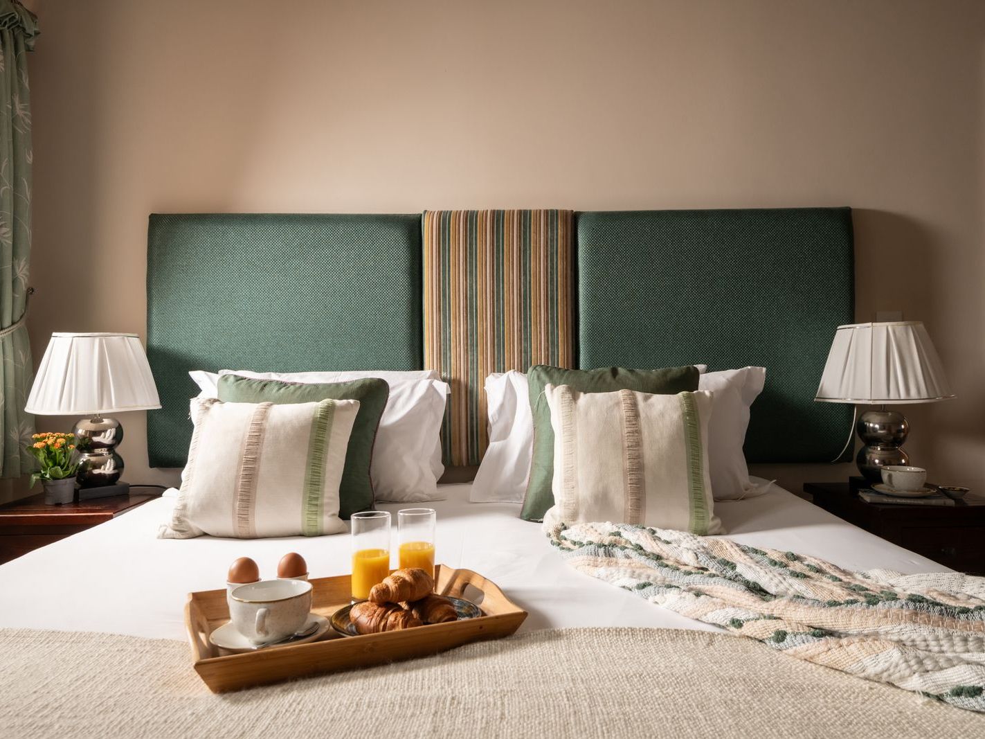 Cozy bedroom with green headboard, breakfast tray on bed, and two bedside lamps