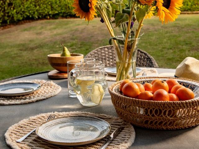Outdoor table set with plates, a pitcher of water, a basket of peaches, and a vase of sunflowers.