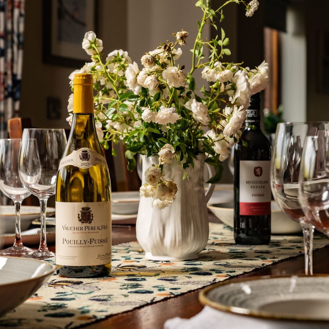 Elegant dining table set with wine bottles, glassware, bowls, and a vase of white flowers.