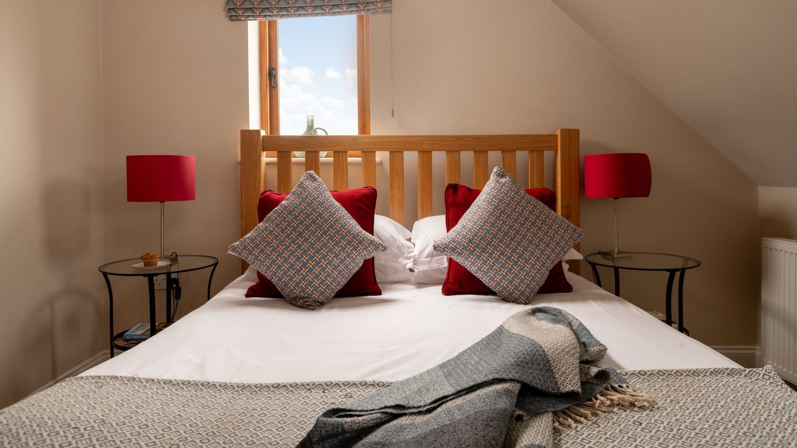 Cozy bedroom with a wooden headboard, colorful pillows, and bedside tables with red lamps.