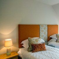 Twin beds with orange headboard and cushions in a bright bedroom
