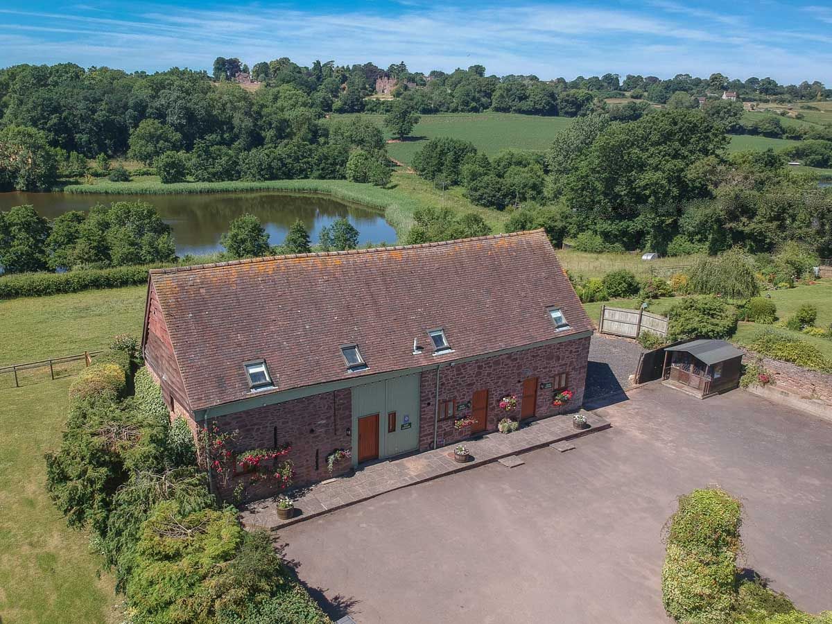 Aerial view of a rustic stone barn surrounded by countryside, trees, and a pond.