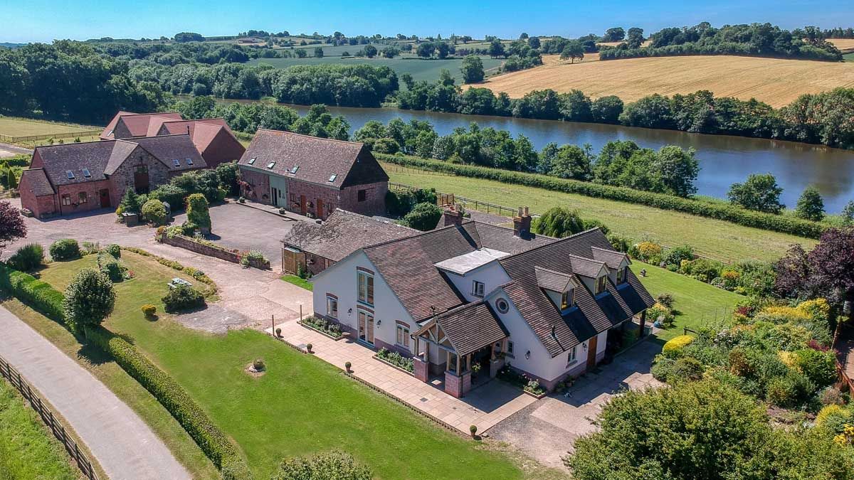 Aerial view of a countryside house with outbuildings, gardens, and a river in the background
