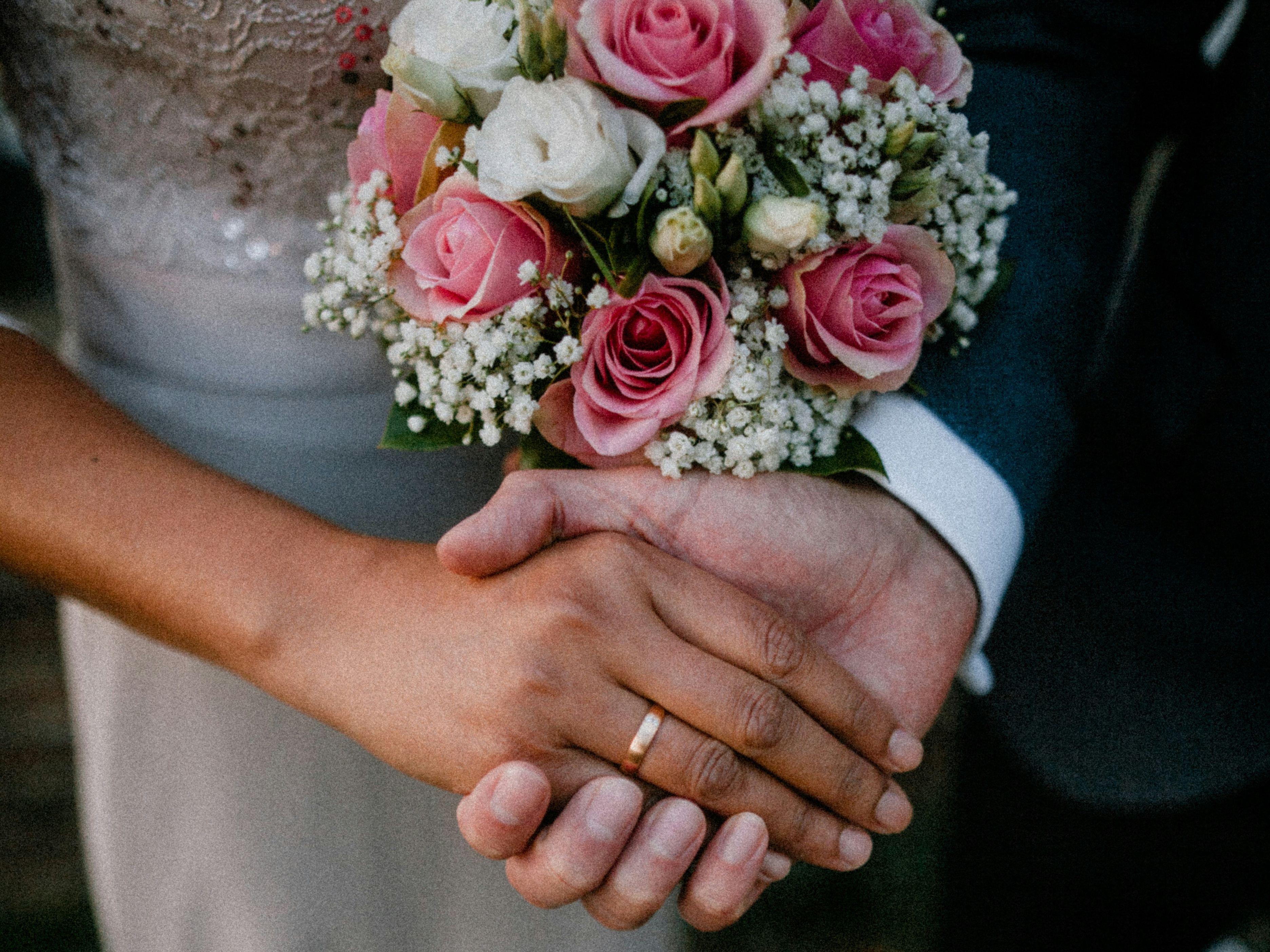 Close-up of bride and groom holding hands, bride holding a bouquet of pink and white flowers.