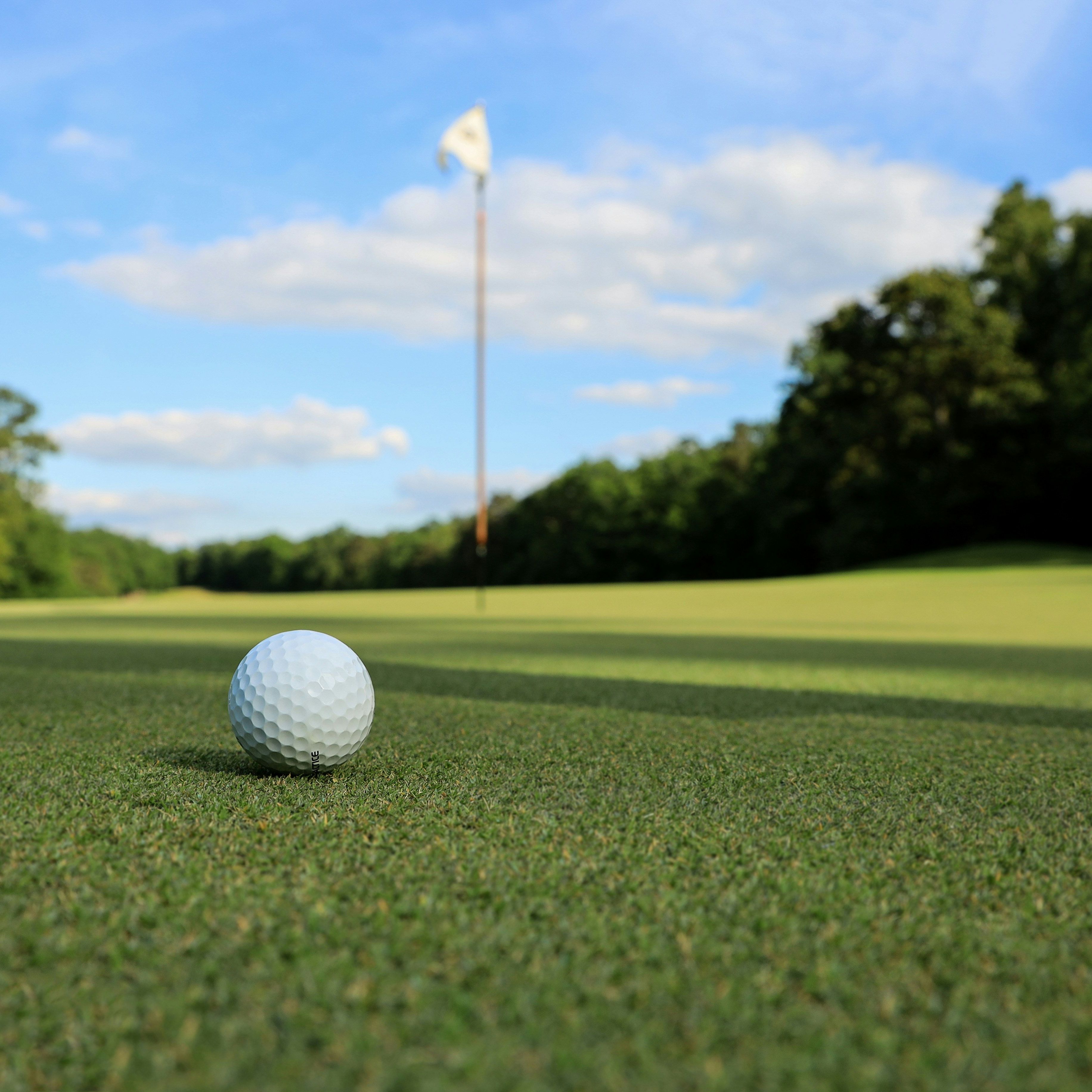Golf ball on green grass near the hole with flag on a golf course