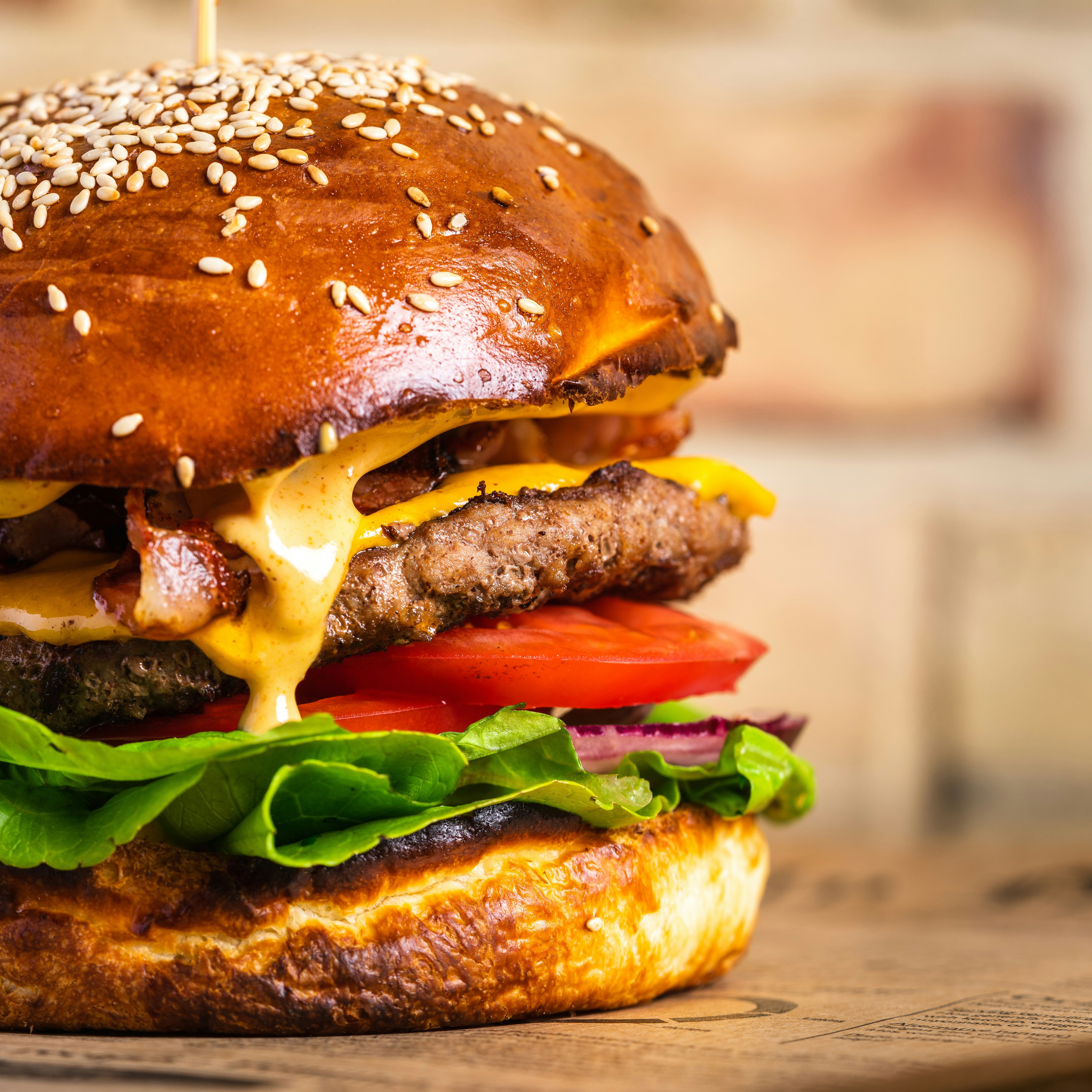 Close-up of a juicy cheeseburger with lettuce, tomato, onion, bacon, melted cheese, and a sesame seed bun.