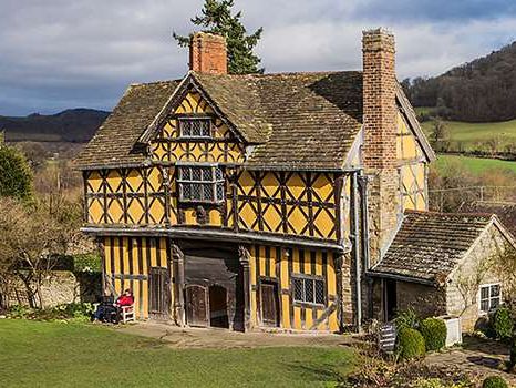 Historic timber-framed building with yellow walls, black beams, and a tiled roof set in the countryside.