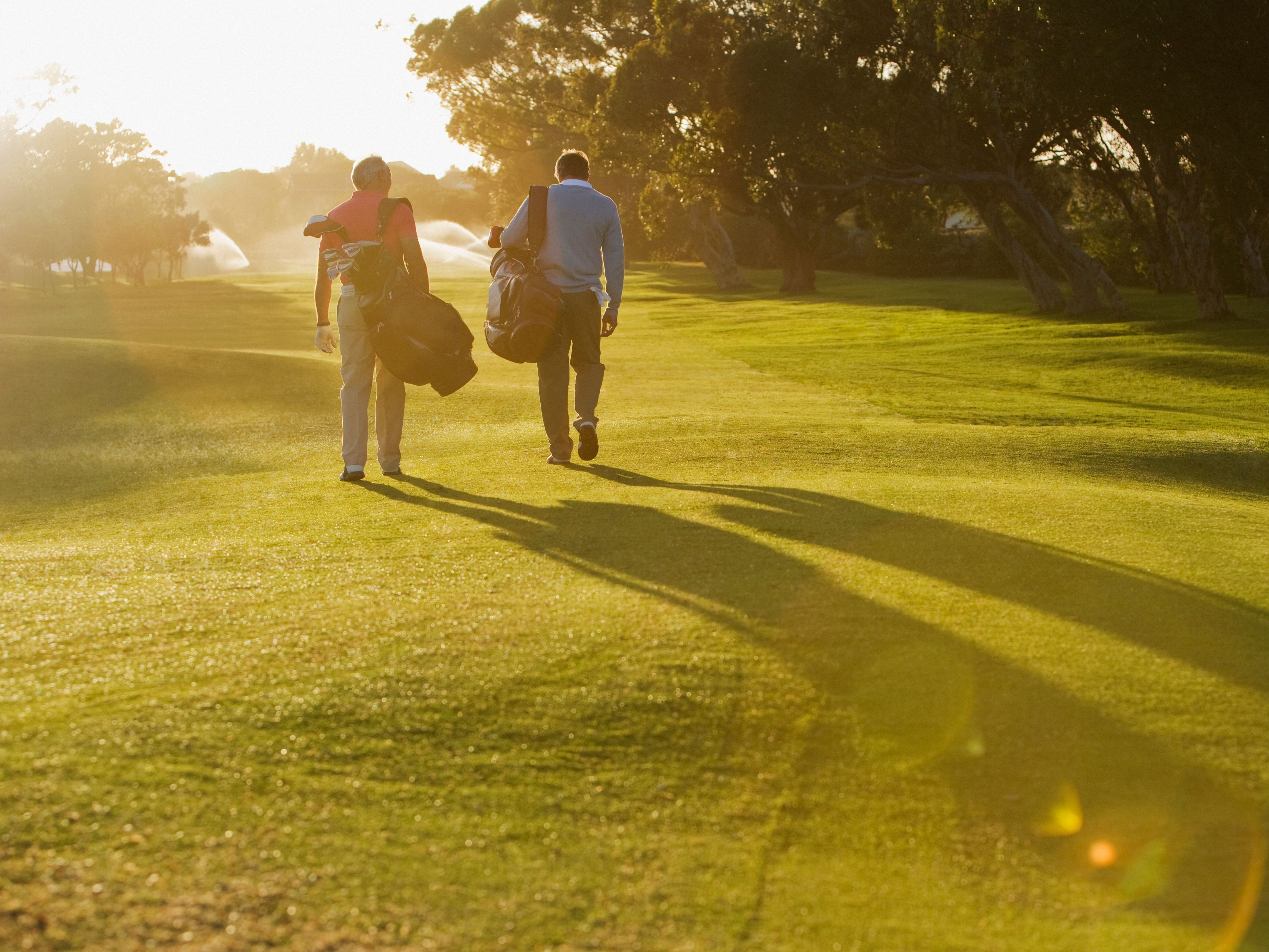 Two people walking on a golf course carrying golf bags during sunset