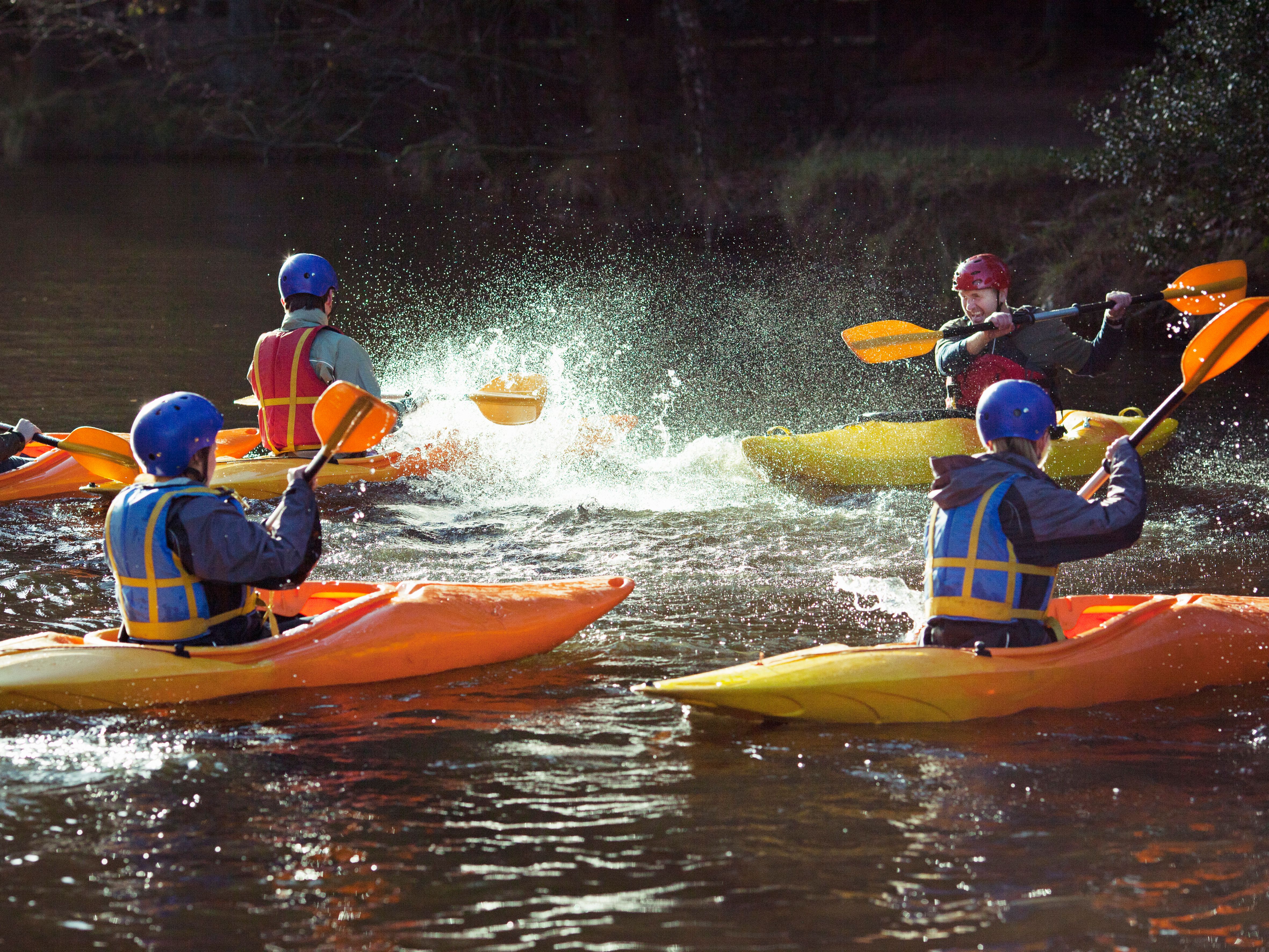 Group of people kayaking on a river, all wearing helmets and life jackets