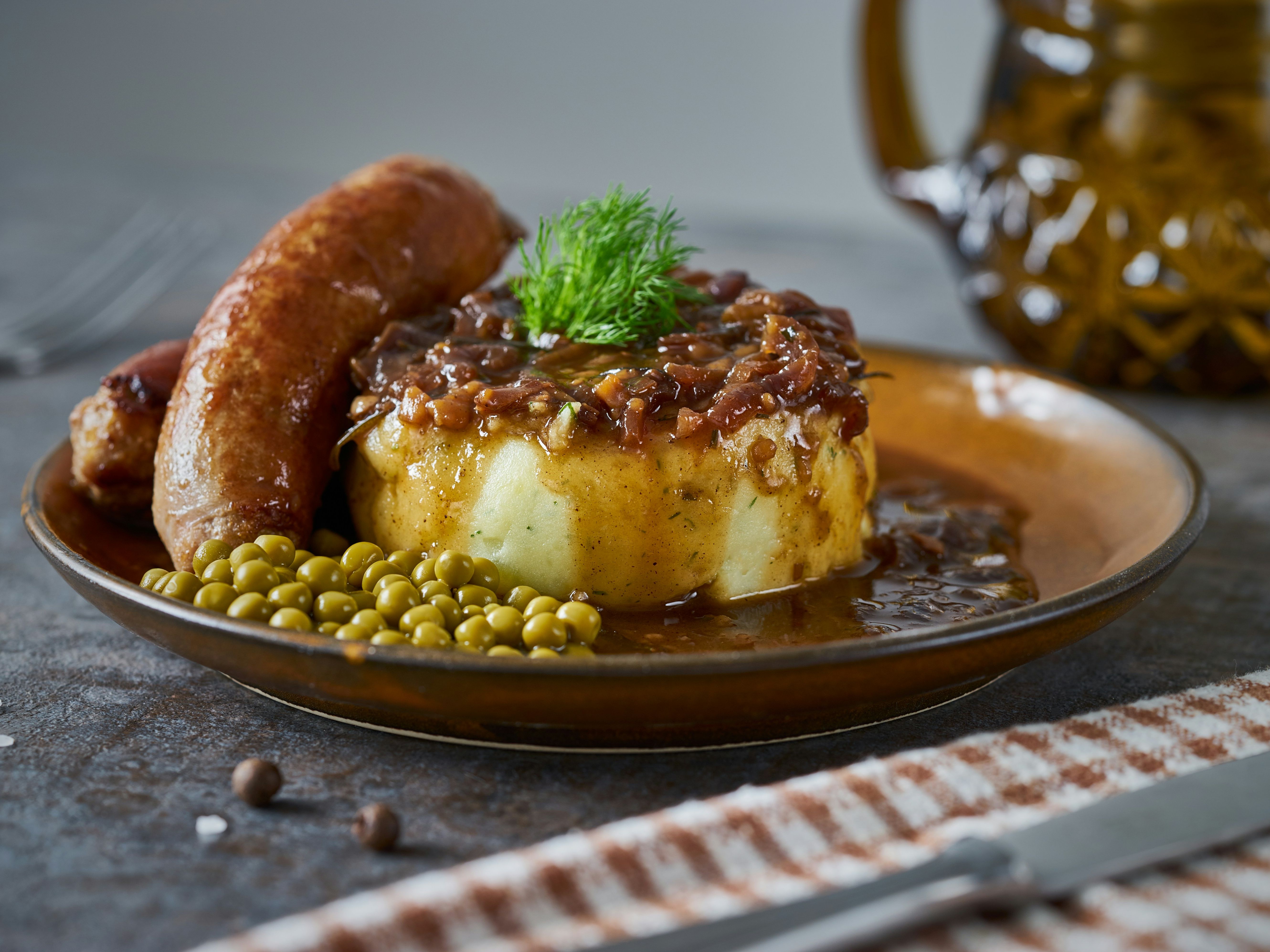 Plate of sausage with mashed potatoes, onion gravy, and green peas