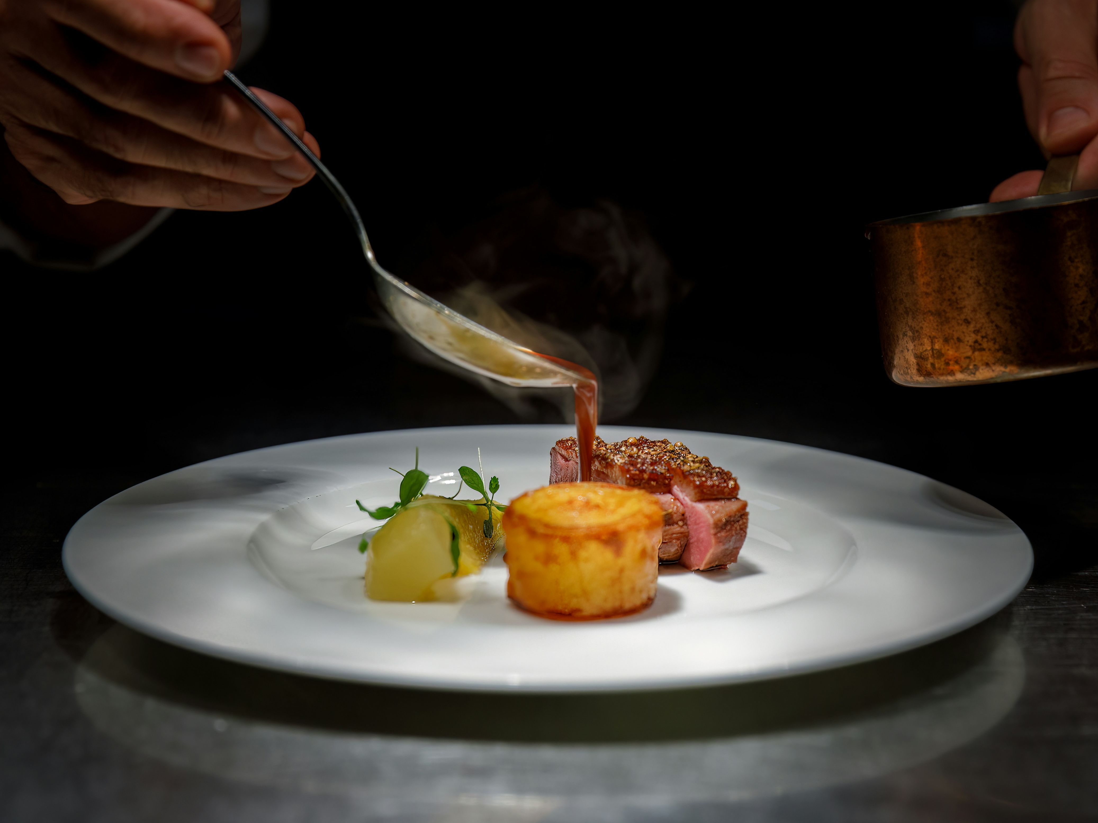 Chef plating gourmet dish with sauce on a white plate