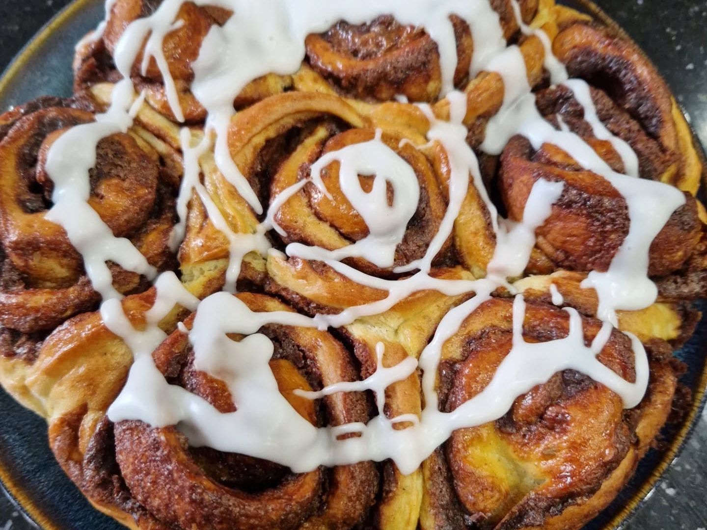 Freshly baked cinnamon buns topped with white icing on a plate.