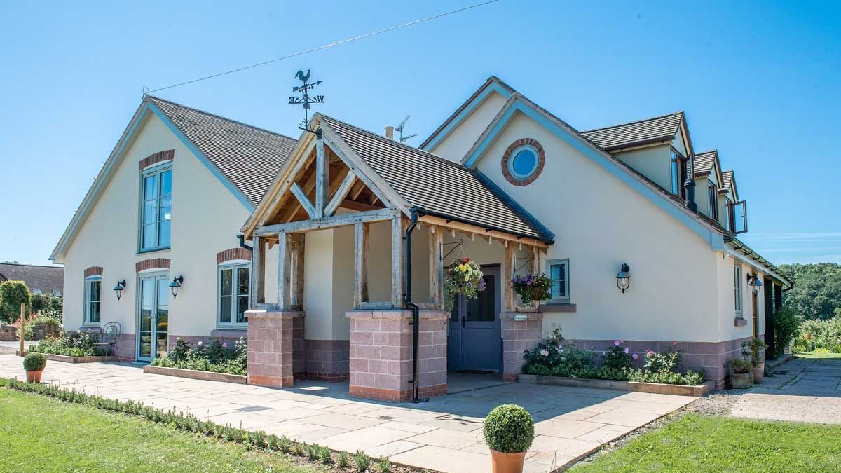 Modern countryside house with timber-framed porch and hanging baskets in a sunny garden