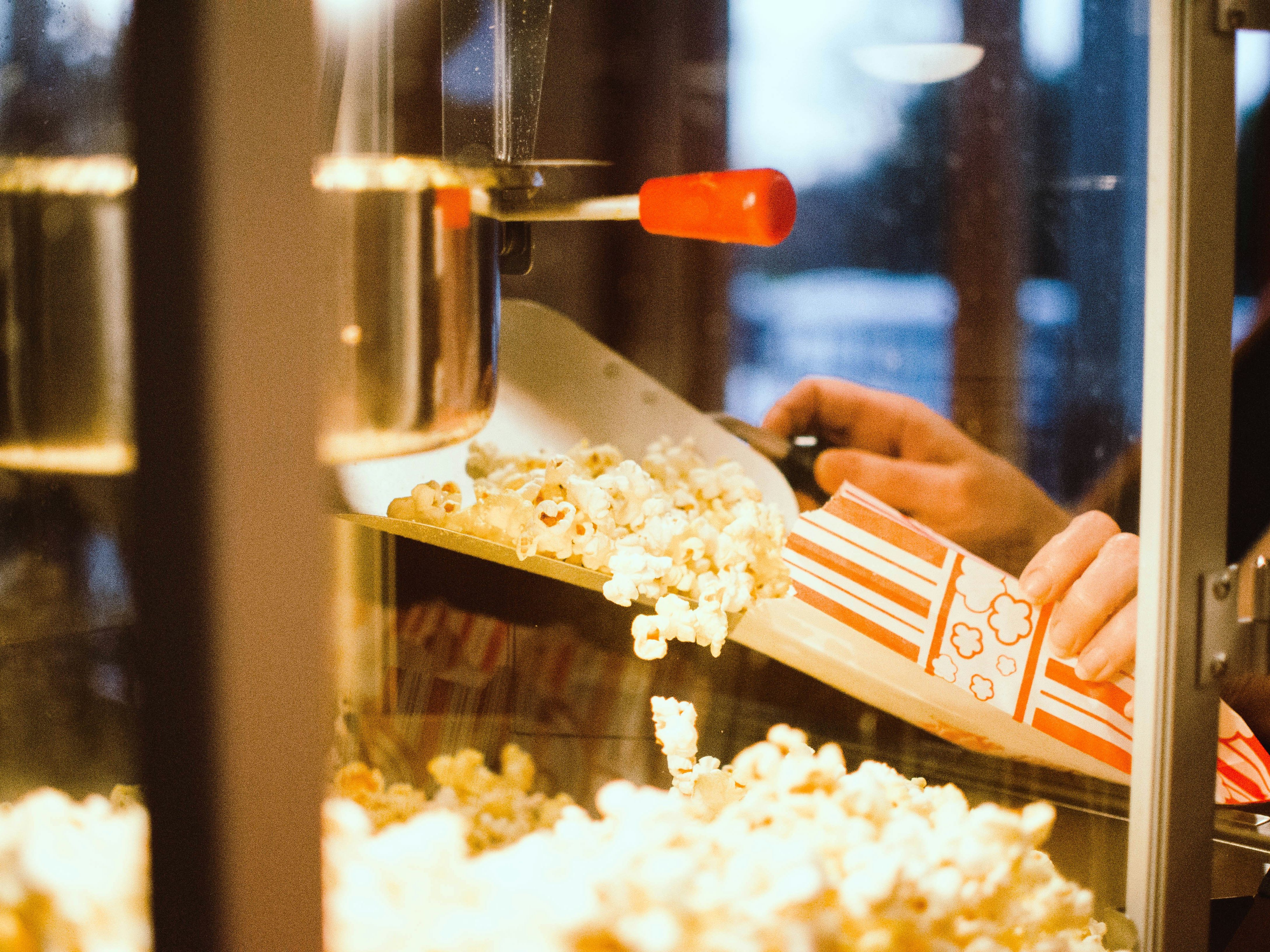 Hand scooping freshly popped popcorn into a striped paper bag from a popcorn machine