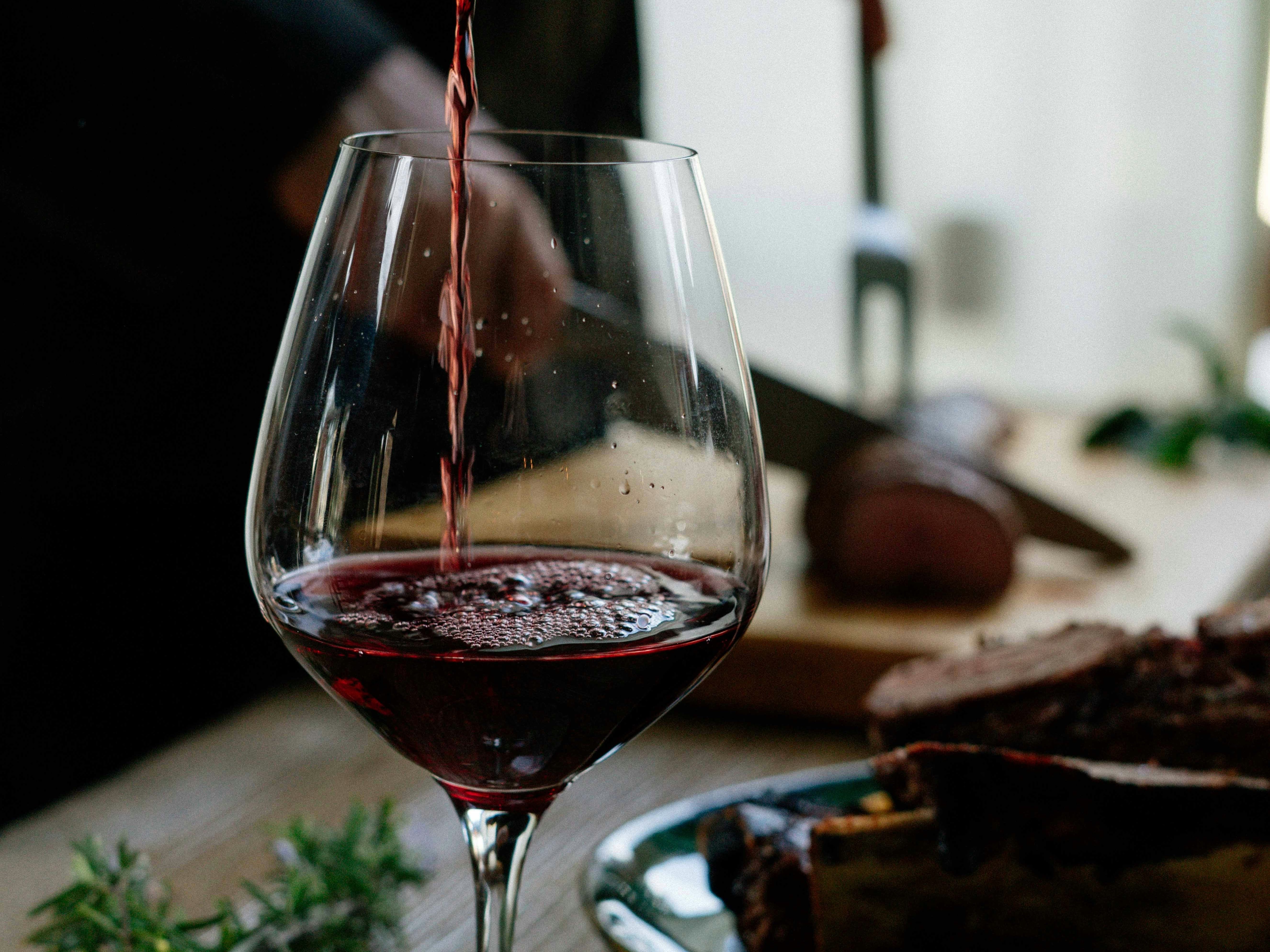 Red wine being poured from a bottle into a glass on a wooden table