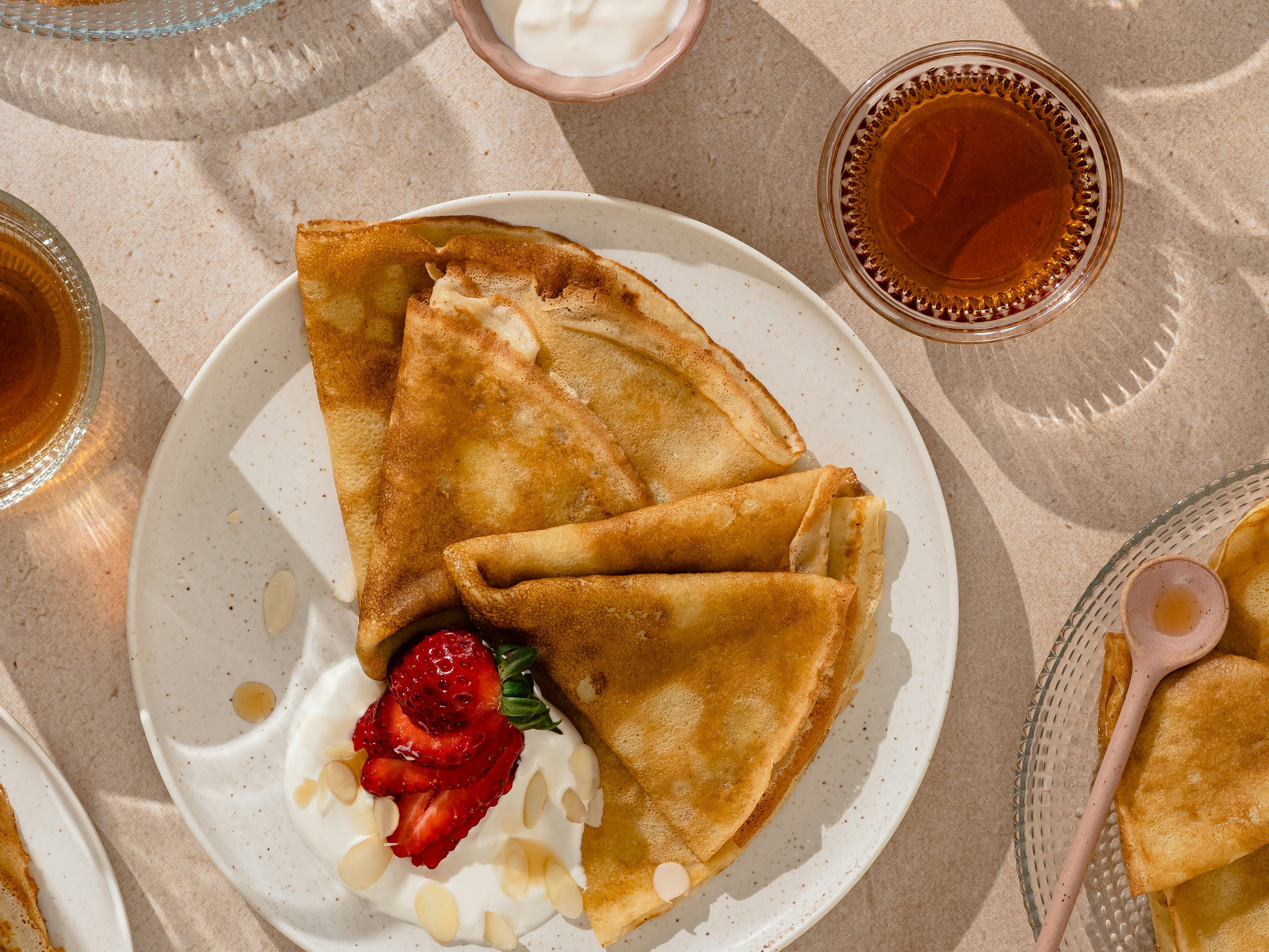 Top-down view of folded crêpes with yoghurt, strawberries and honey alongside glasses of tea