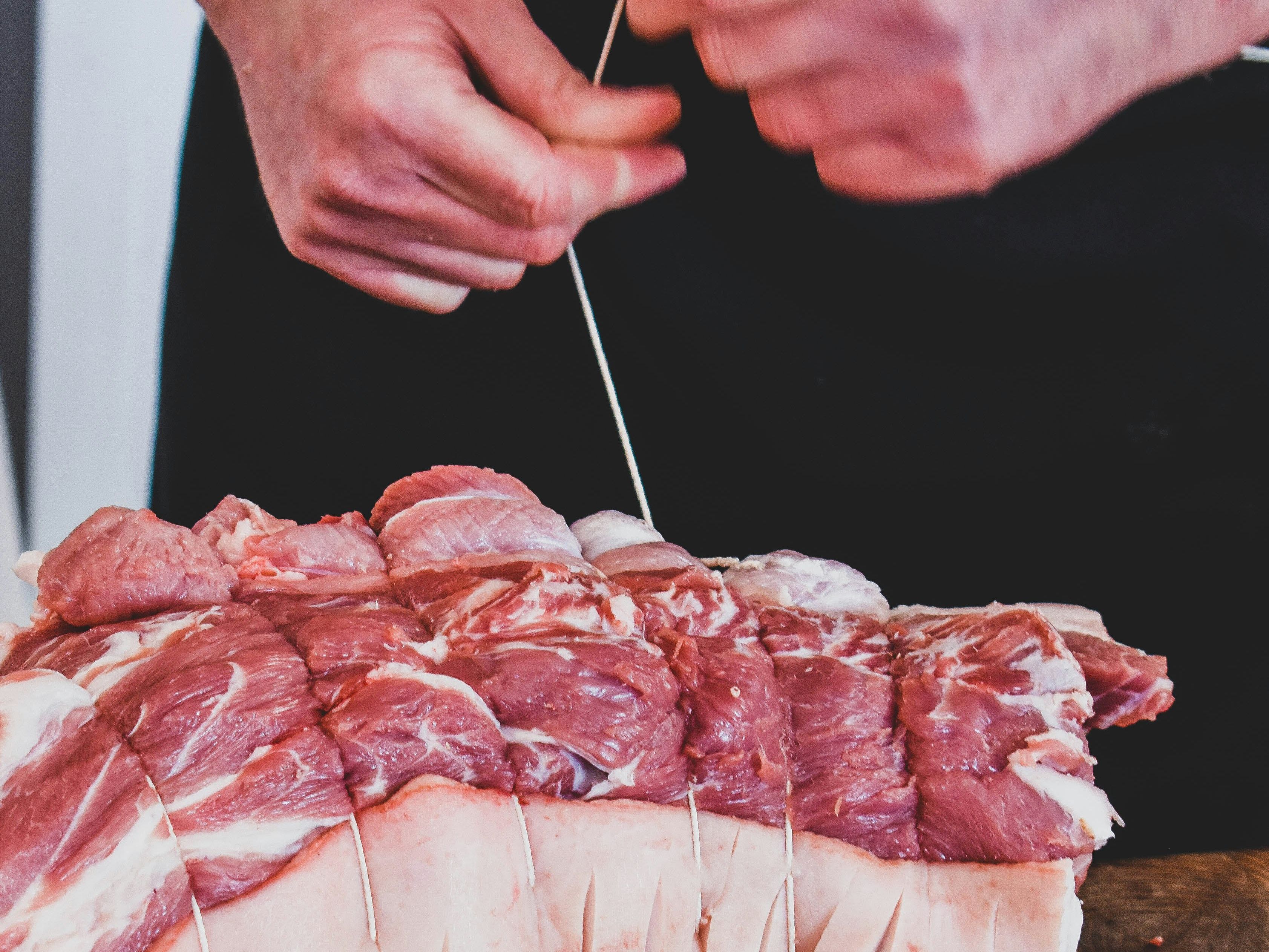 Hands tying butcher’s string around a rolled pork joint on a wooden board