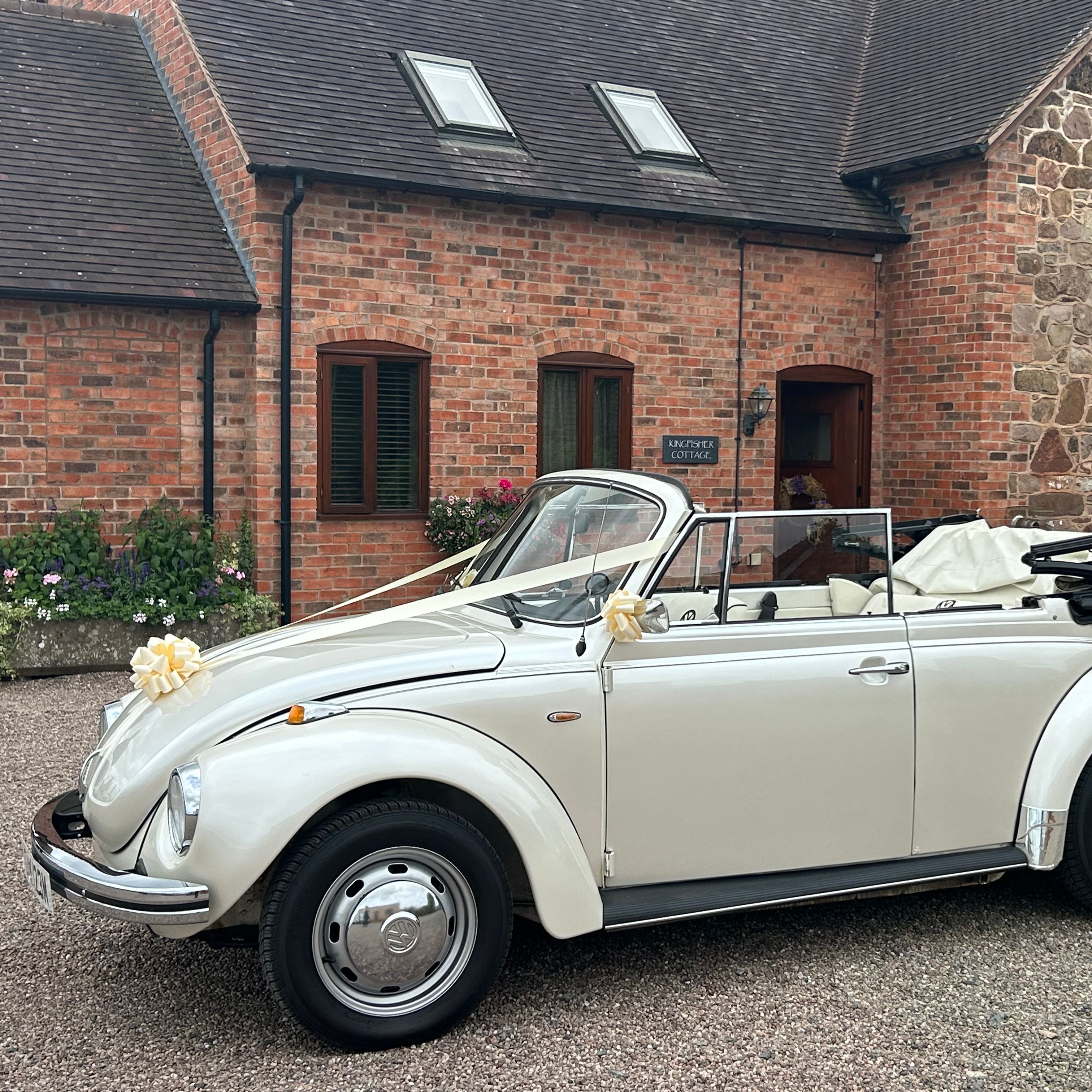 White vintage convertible car decorated with ribbons, parked outside a brick and stone cottage