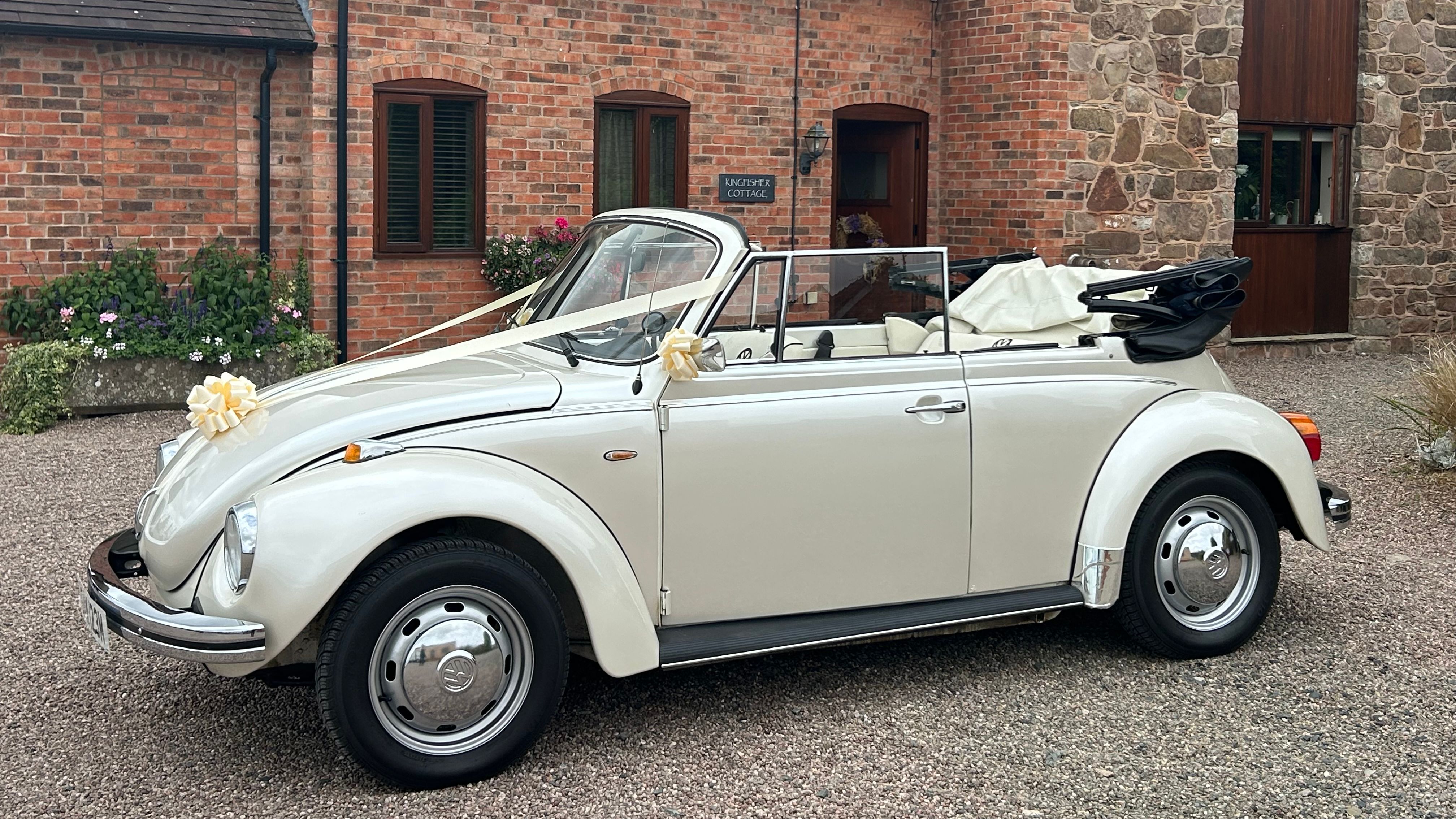 White vintage convertible car decorated with ribbons, parked outside a brick and stone cottage