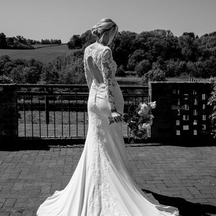 Bride in a lace wedding dress holding a bouquet, standing outdoors with countryside in the background