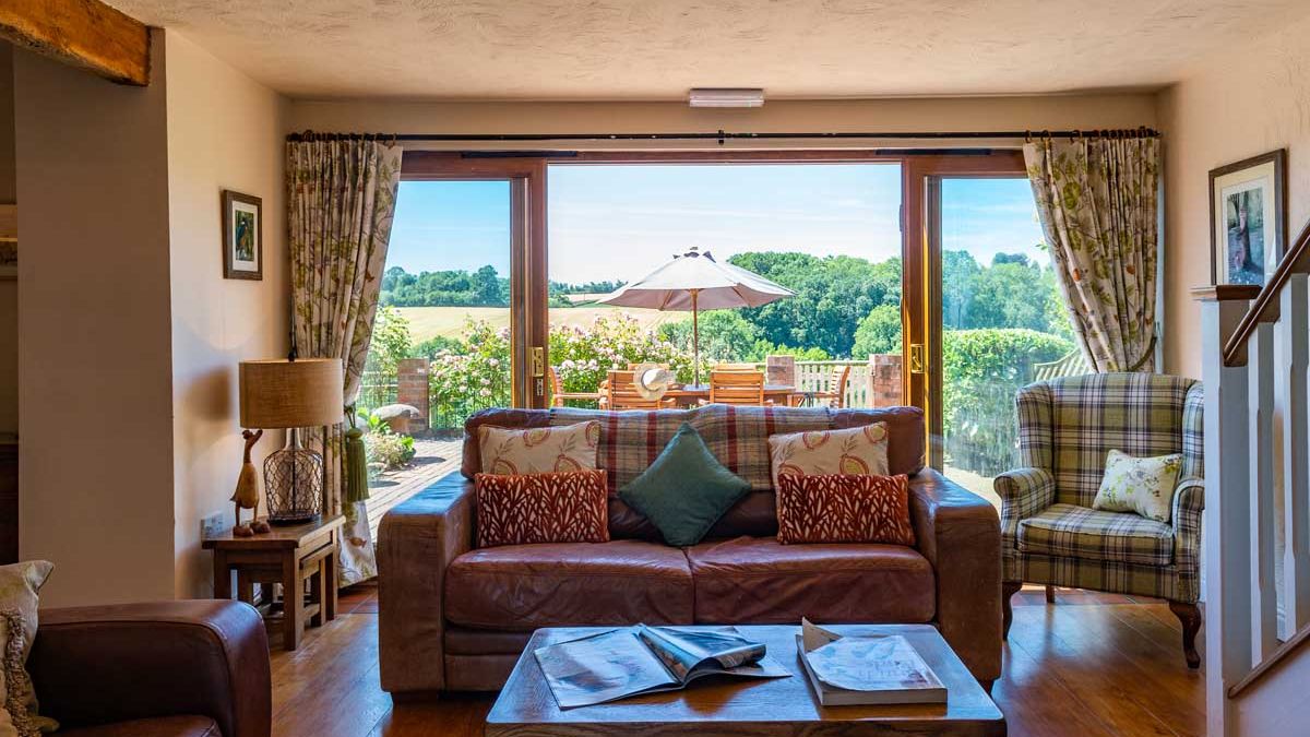 Cozy living room with sofa, coffee table, armchair, and view of a garden patio through large glass doors.