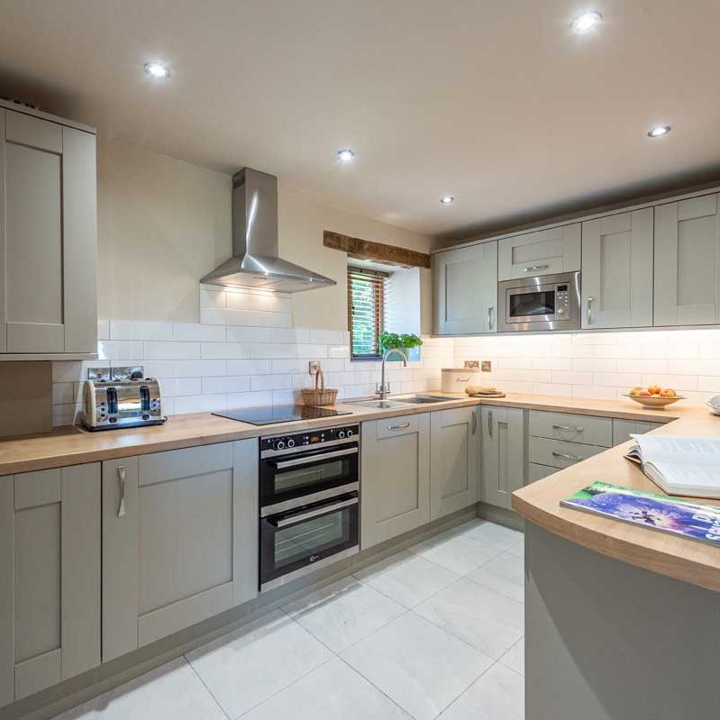 Modern kitchen with light grey cabinets, wooden countertops, and stainless steel appliances.