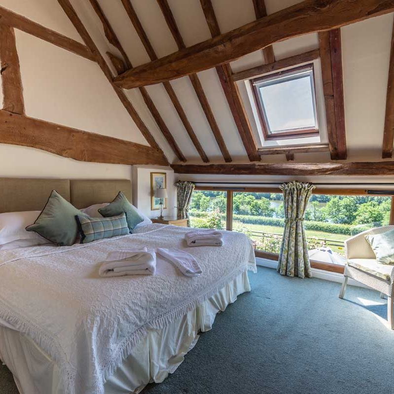 Cozy attic bedroom with exposed wooden beams, large bed, skylight, and scenic window view.