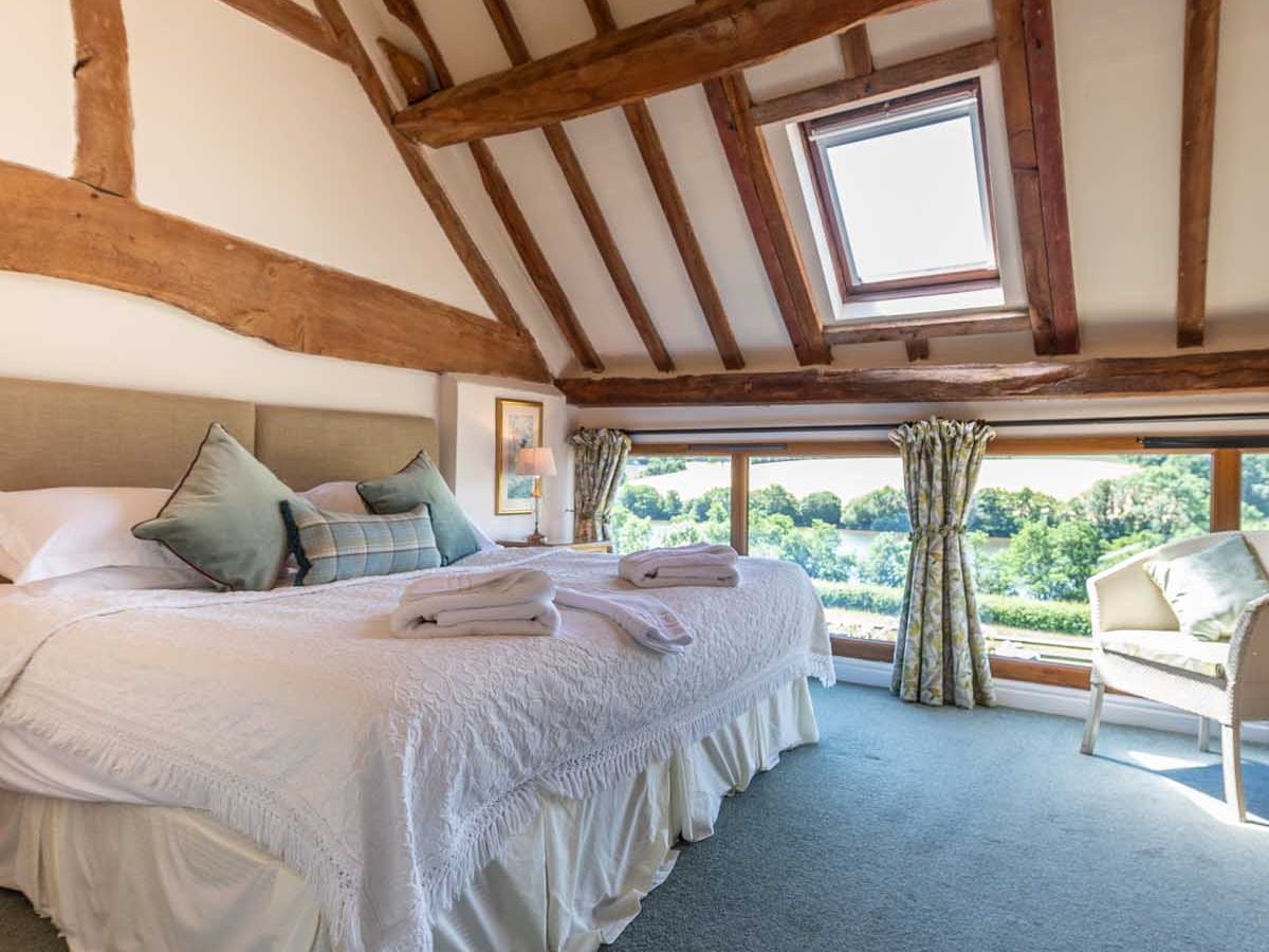 Cozy attic bedroom with exposed wooden beams, large bed, skylight, and scenic window view.