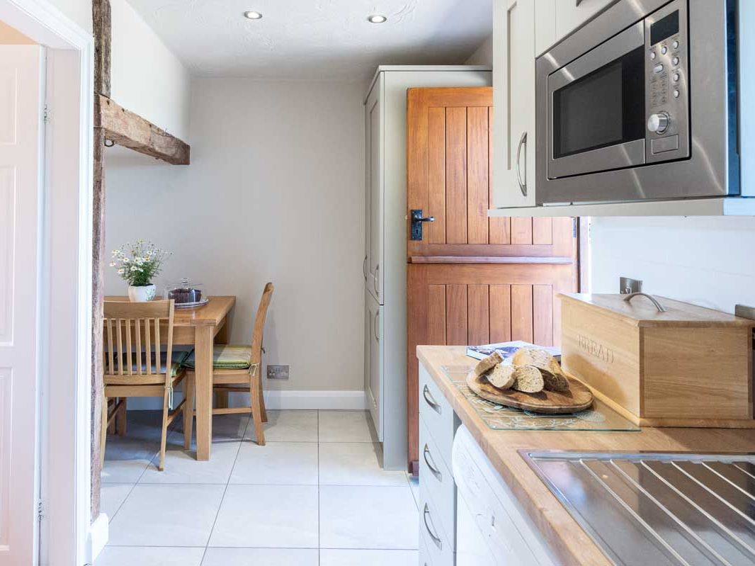 Bright kitchen with wooden accents, featuring a dining table, microwave, and bread on the counter.