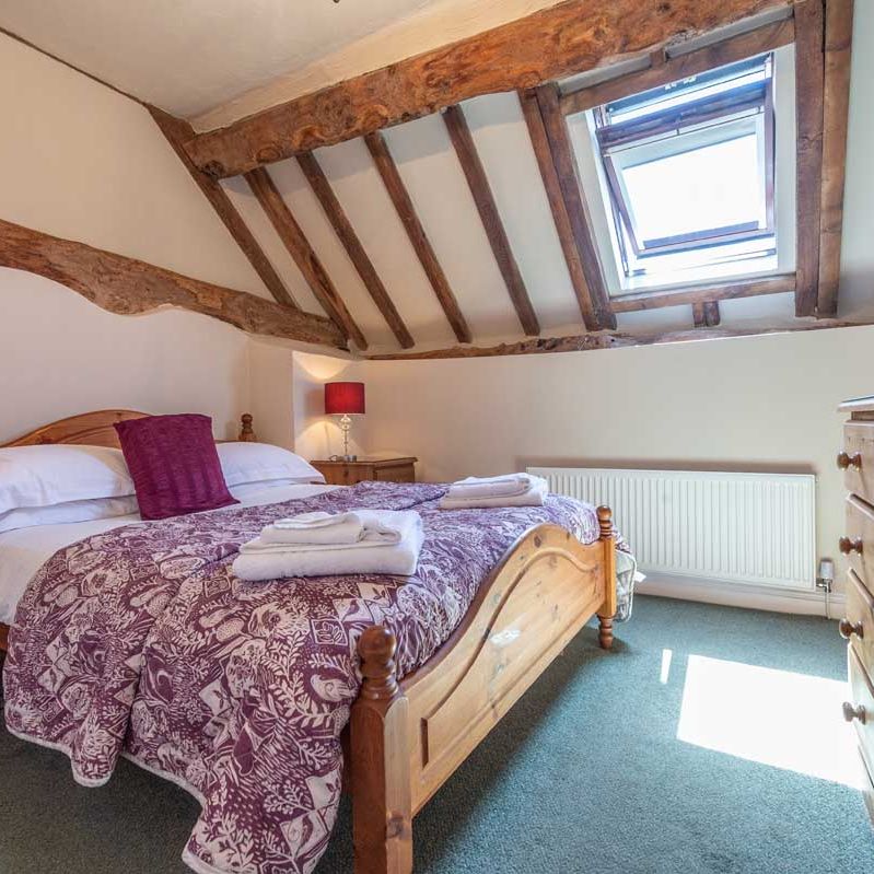 Cozy attic bedroom with wooden beams, skylight, and a double bed.