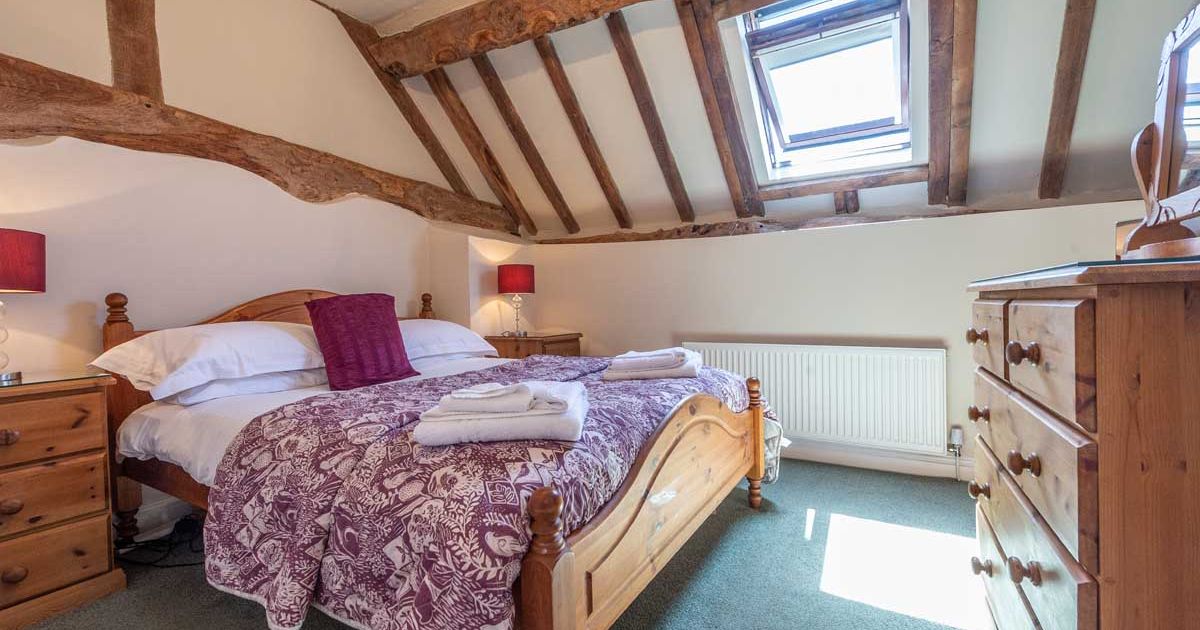 Cozy attic bedroom with wooden beams, skylight, and a double bed.